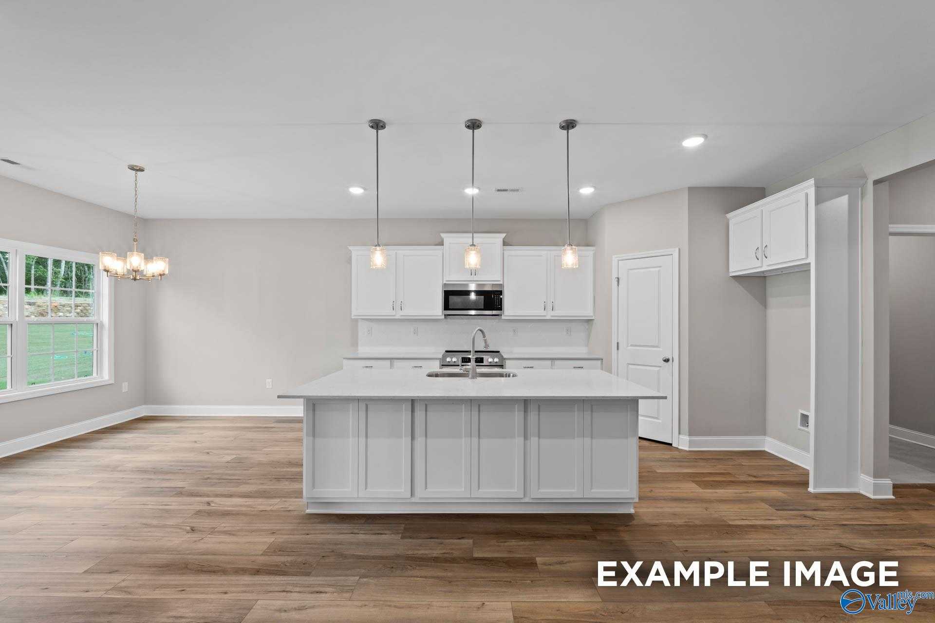 Bright modern kitchen with white shaker cabinets, large island sink, and open layout in The Montgomery 3-bedroom home, Meridianville, Alabama