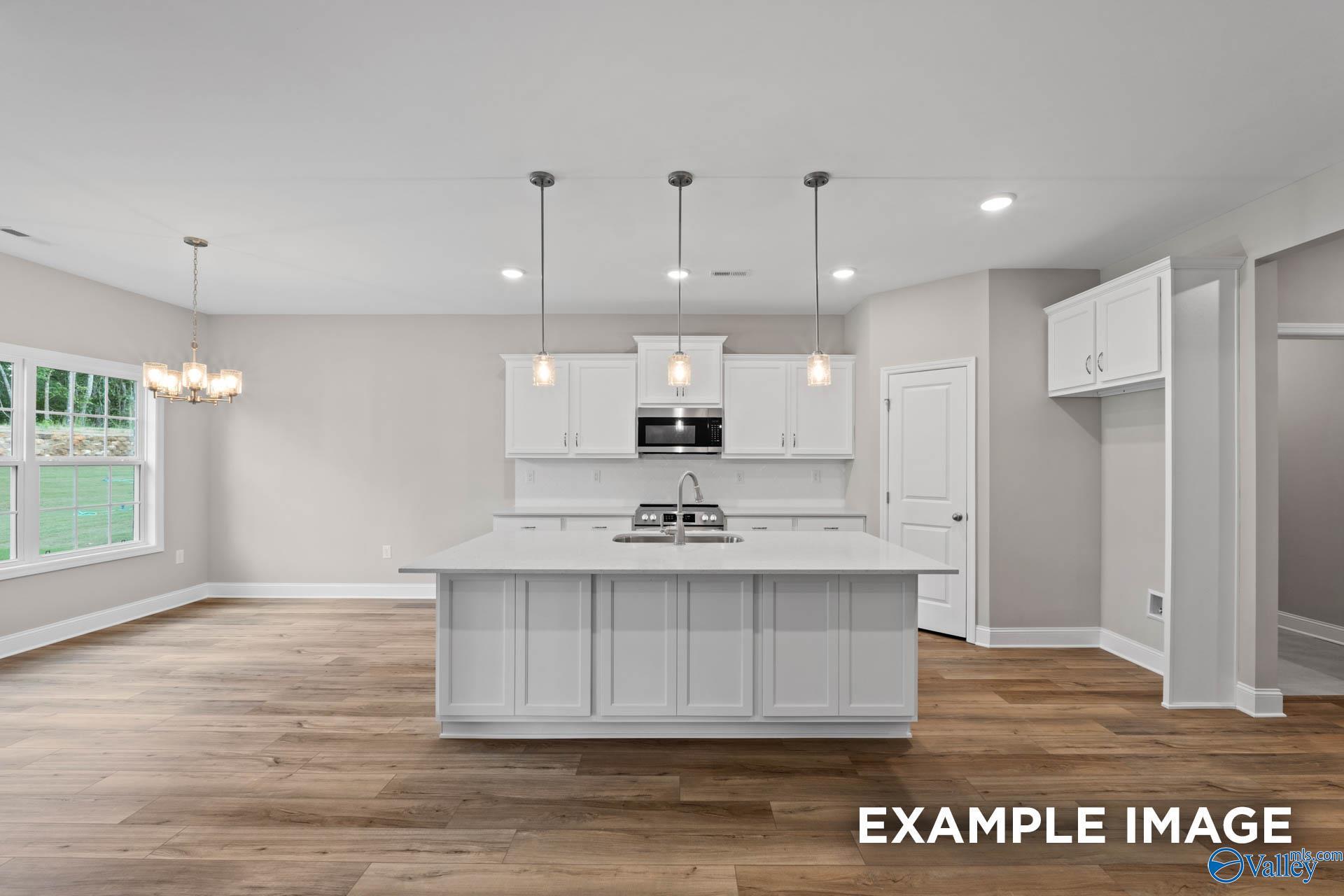 Bright modern kitchen with white shaker cabinets, large island sink, and open layout in The Montgomery 3-bedroom home, Meridianville, Alabama