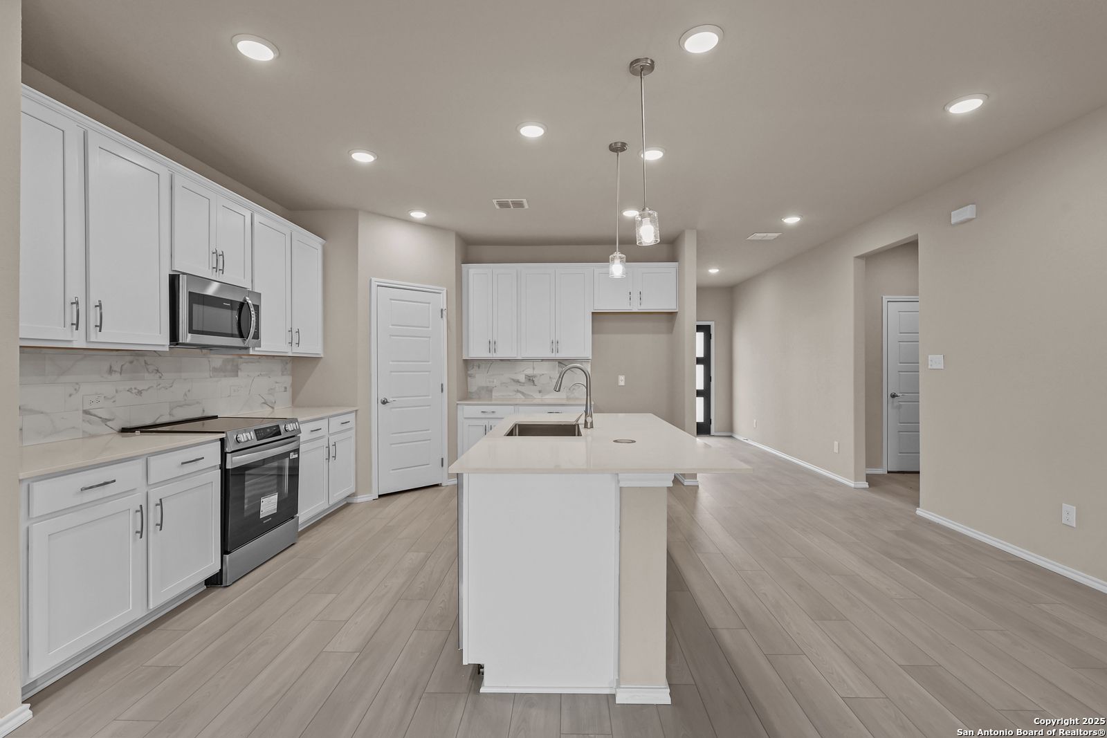 Modern white kitchen with stainless appliances, large island sink, subway tile backsplash in Davidson Homes The Douglas G, San Antonio