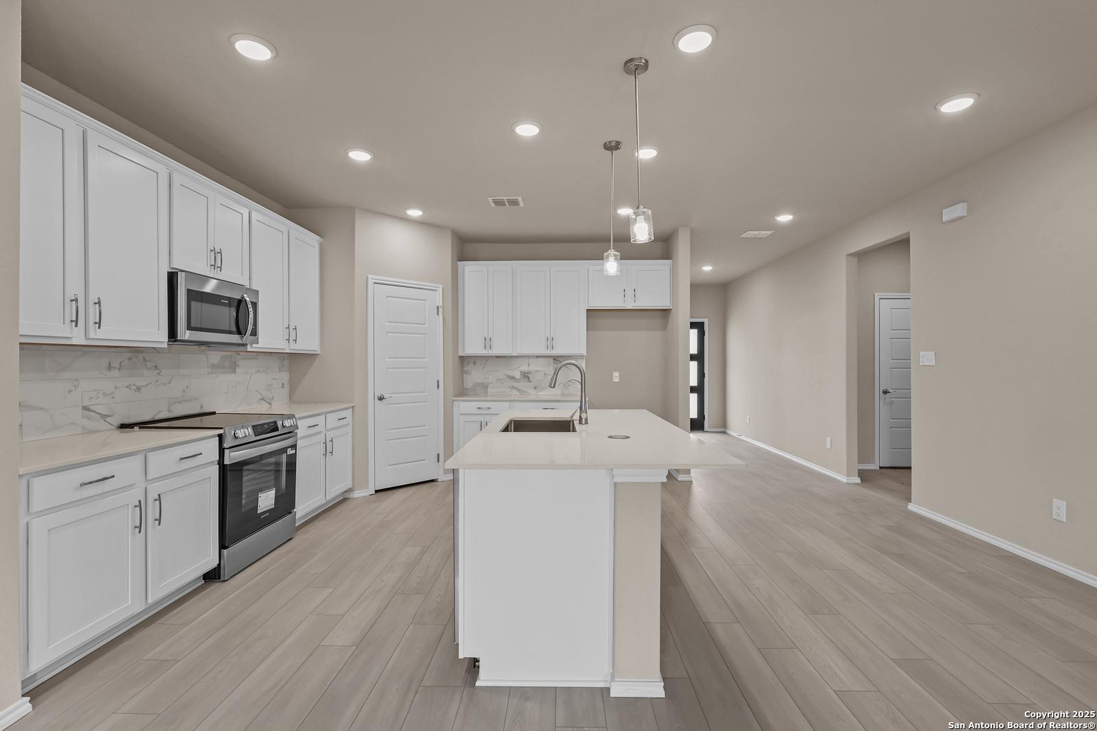 Modern white kitchen with stainless appliances, large island sink, subway tile backsplash in Davidson Homes The Douglas G, San Antonio
