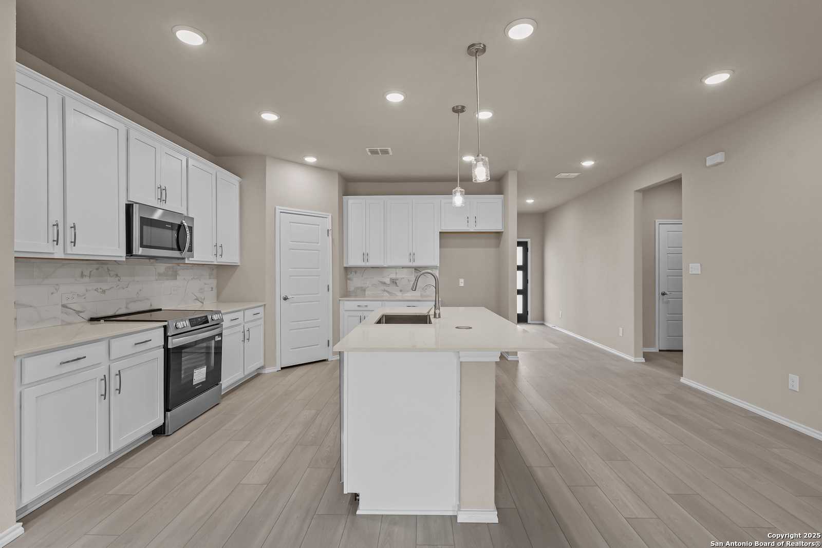 Modern white kitchen with stainless appliances, large island sink, subway tile backsplash in Davidson Homes The Douglas G, San Antonio
