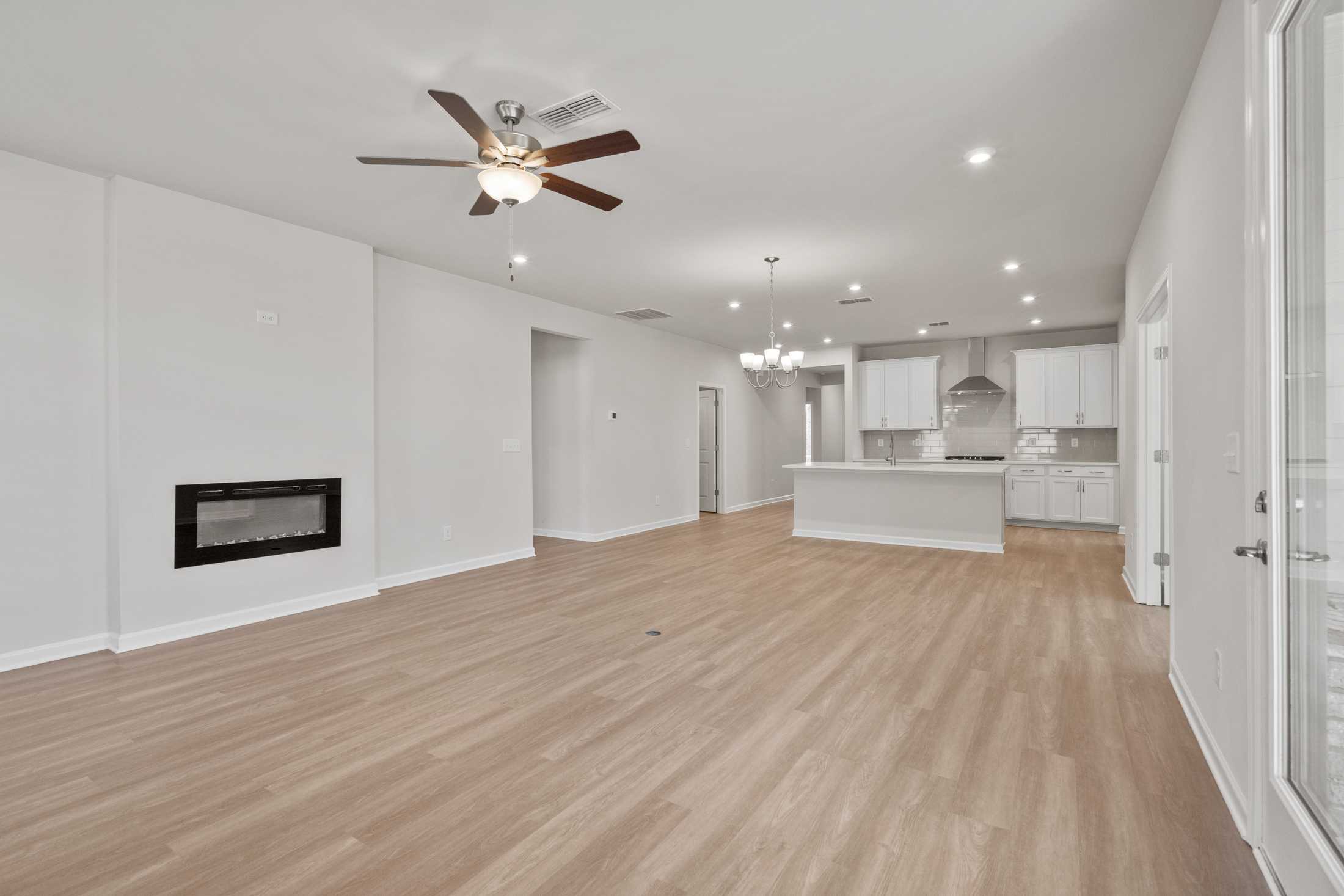 Spacious open-concept living room and kitchen in The Dawson B featuring white island, gas fireplace, and hardwood floors