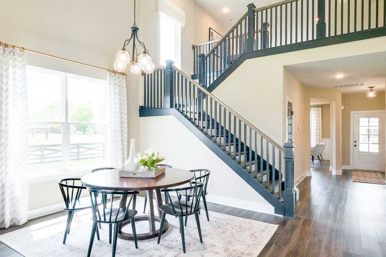 Spacious open-concept dining area in The Meadows Smyrna TN home by Davidson Homes with round wooden table, navy staircase and large windows