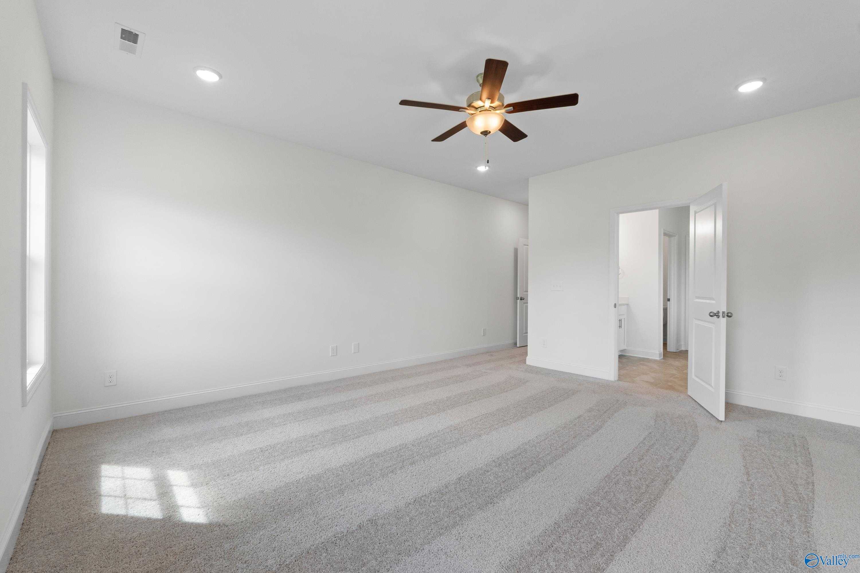 Spacious empty bedroom with white walls, beige carpet, ceiling fan, and natural light in Davidson Homes The Rockford B, Toney, Alabama