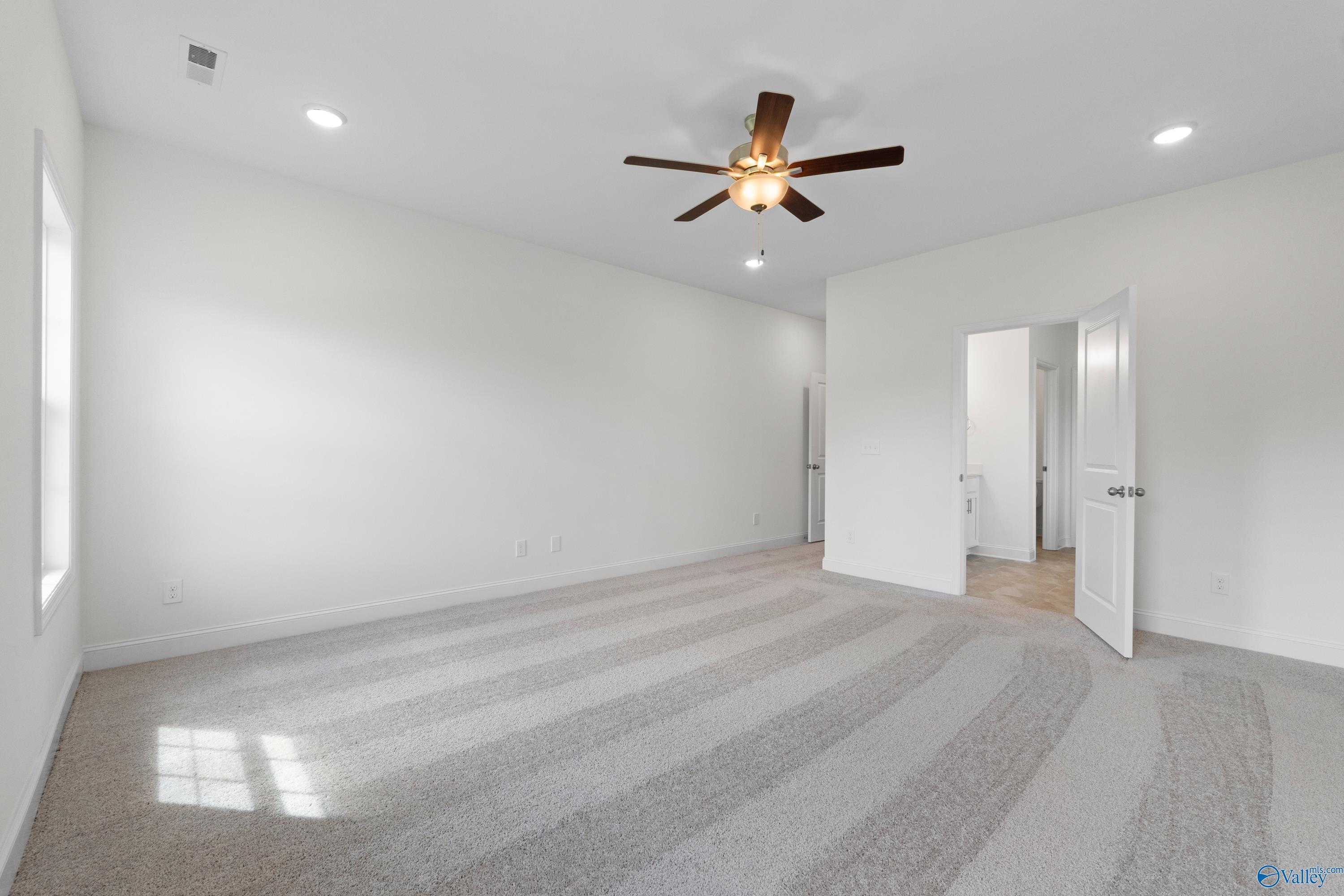Spacious empty bedroom with white walls, beige carpet, ceiling fan, and natural light in Davidson Homes The Rockford B, Toney, Alabama