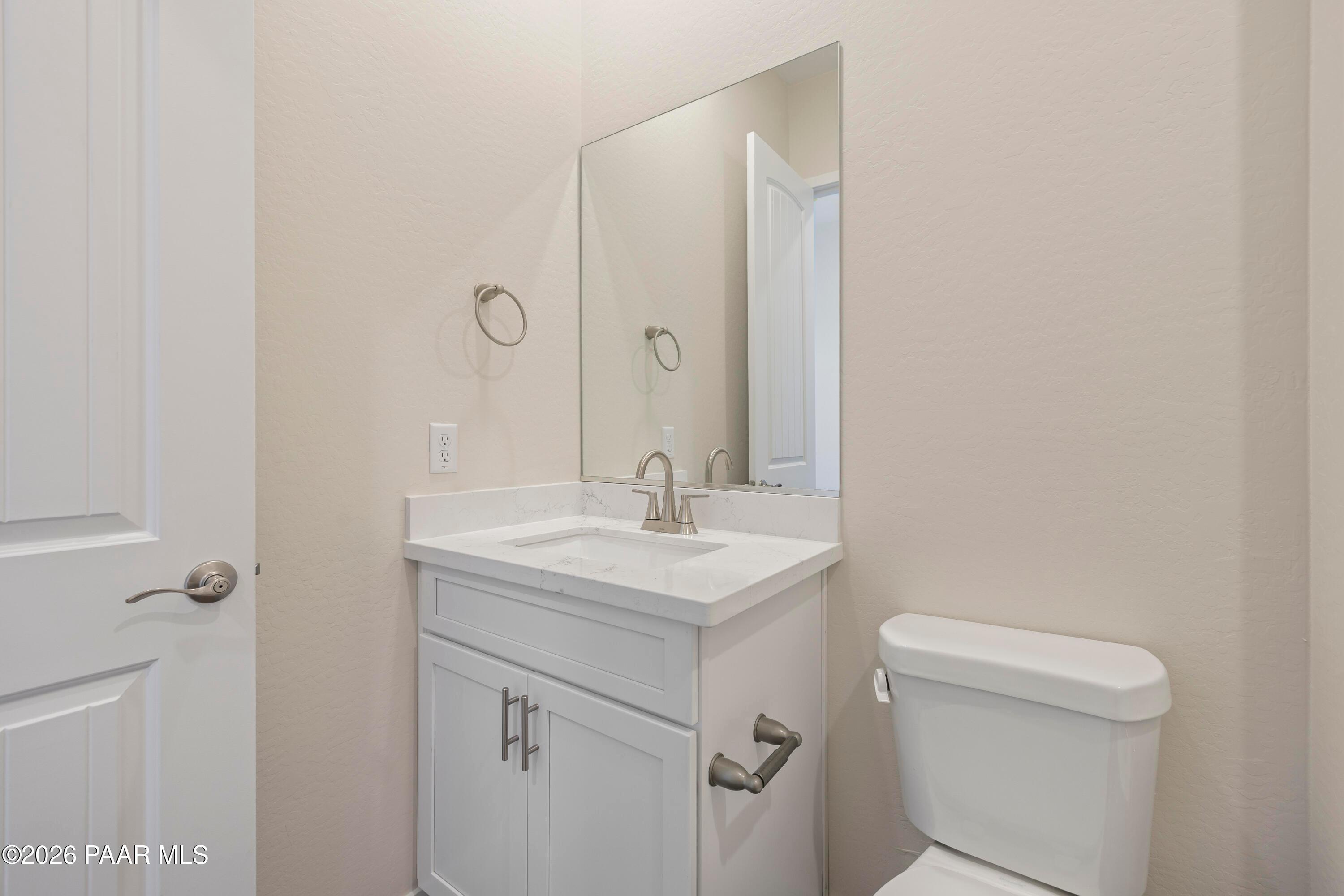 Modern bathroom with white vanity, single sink, large mirror, and toilet in Davidson Homes The Soleil E, Prescott, Arizona