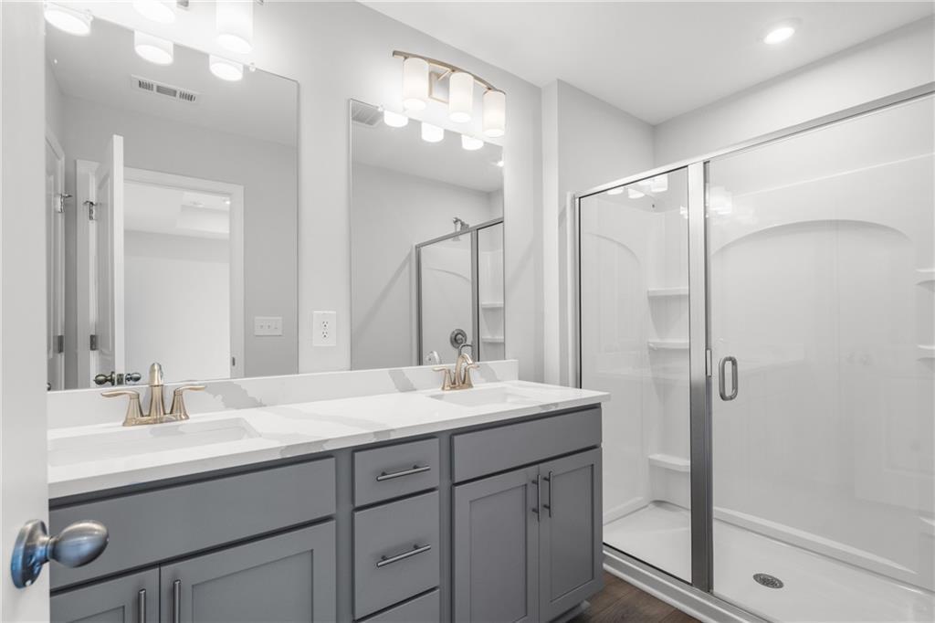 Modern master bathroom featuring double vanity with gray cabinets, white quartz counters, and frameless glass shower in Davidson Homes The Monroe B, Emerson, GA