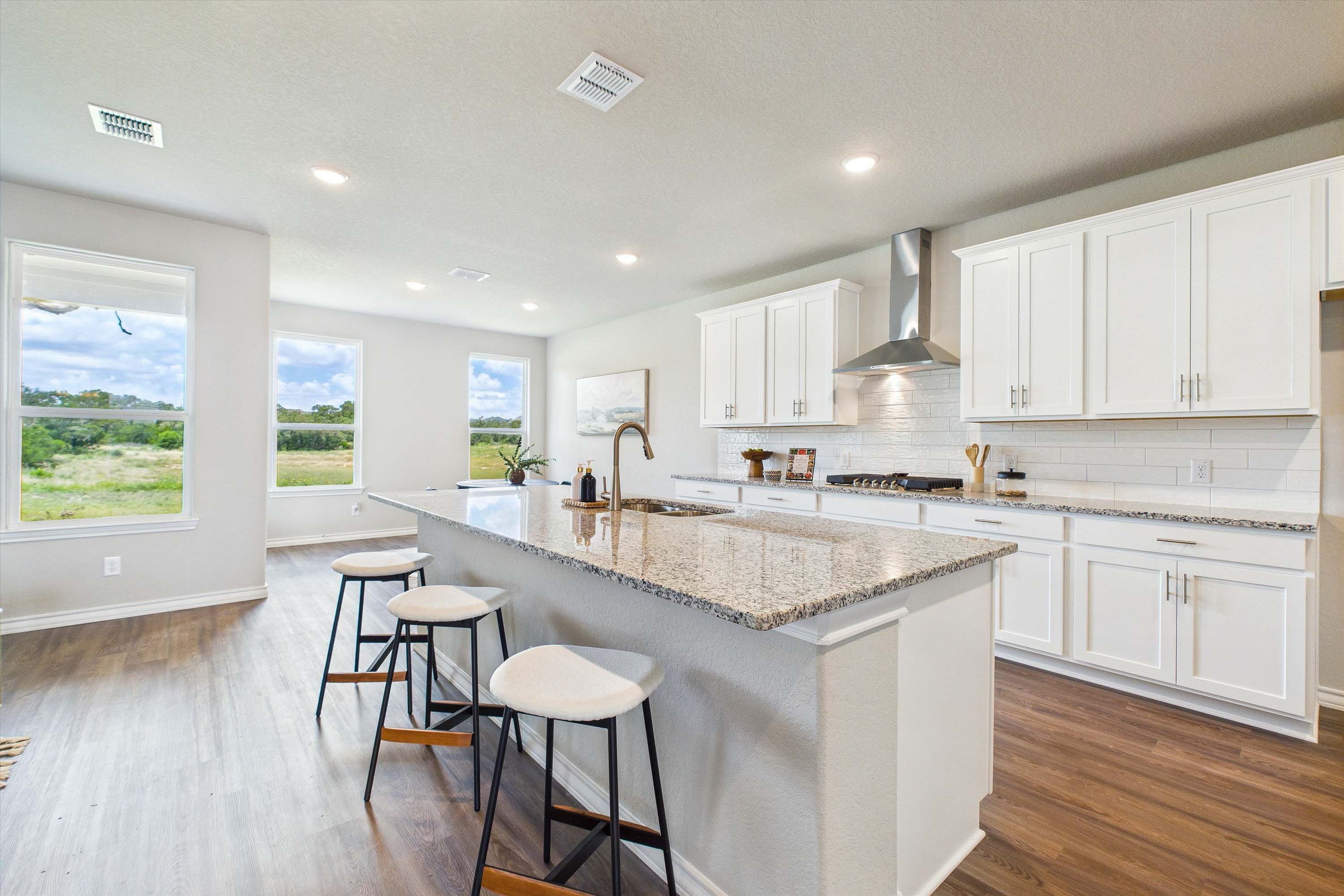 Modern kitchen in The Foster with white cabinetry, granite island, and open-concept dining in Castroville, Texas.