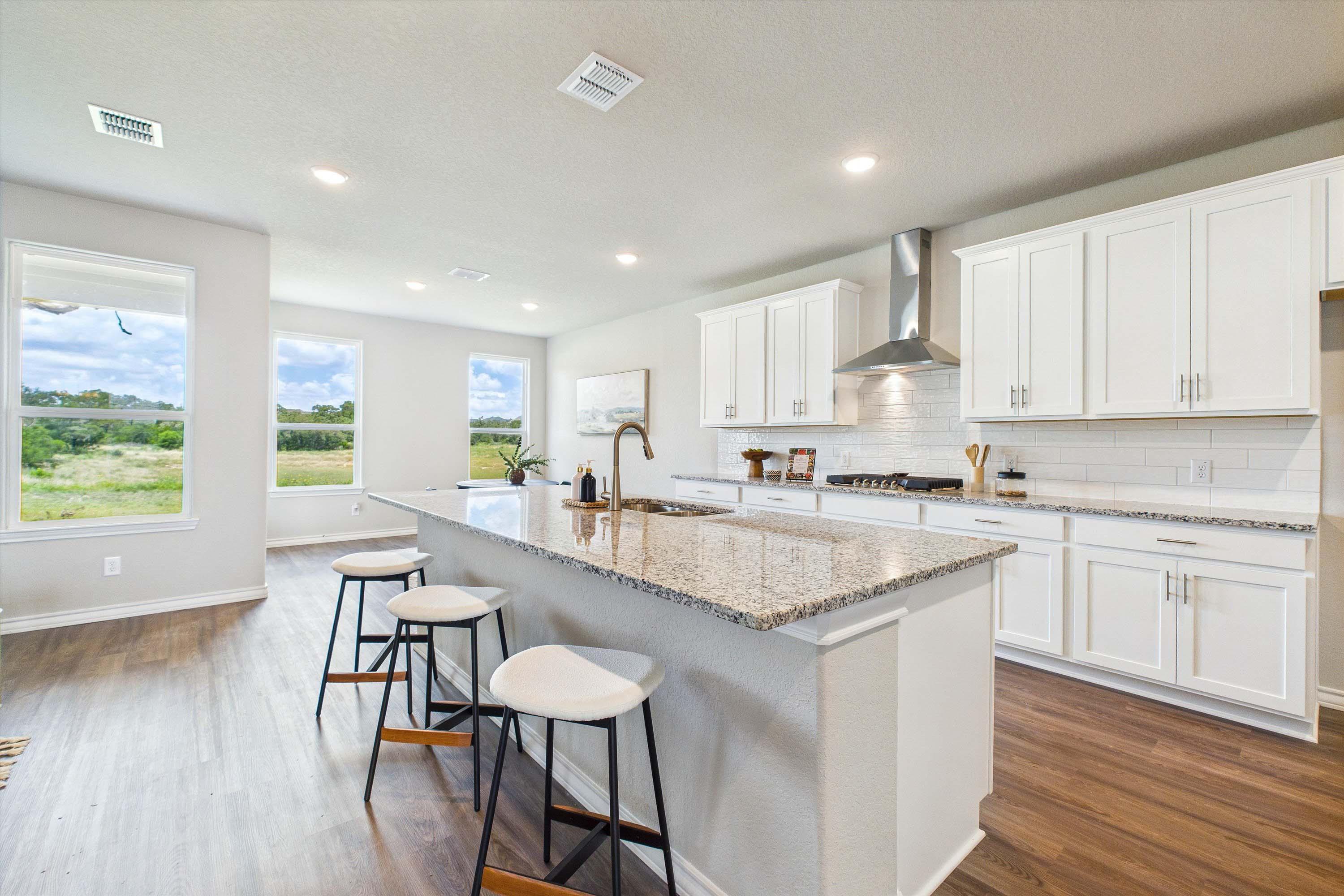 Modern kitchen in The Foster with white cabinetry, granite island, and open-concept dining in Castroville, Texas.