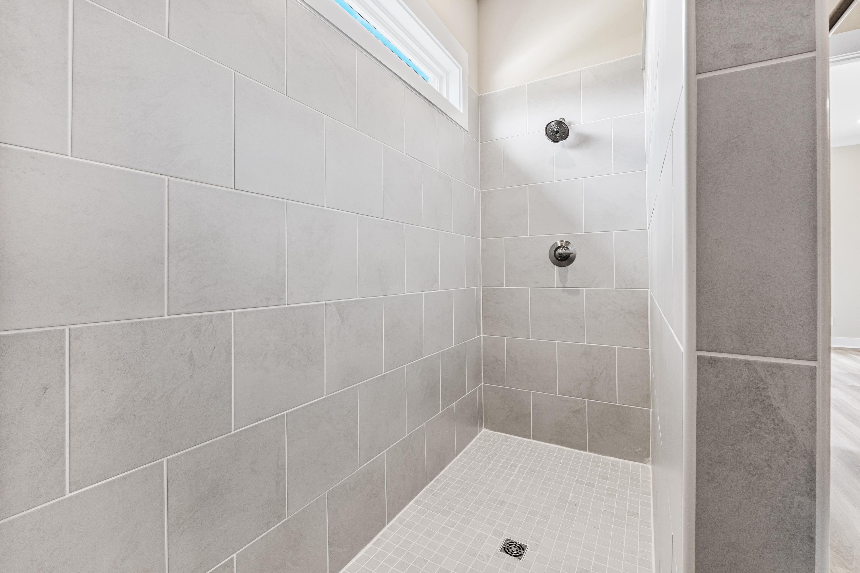 Spacious master shower in The Oxford A with gray subway tile walls, dual showerheads, and frameless glass entry