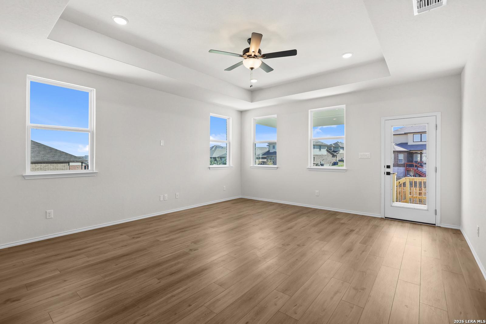 Bright open-concept living room with wood-look flooring, tray ceiling, and glass back door in Davidson Homes' Glenwood E, San Antonio