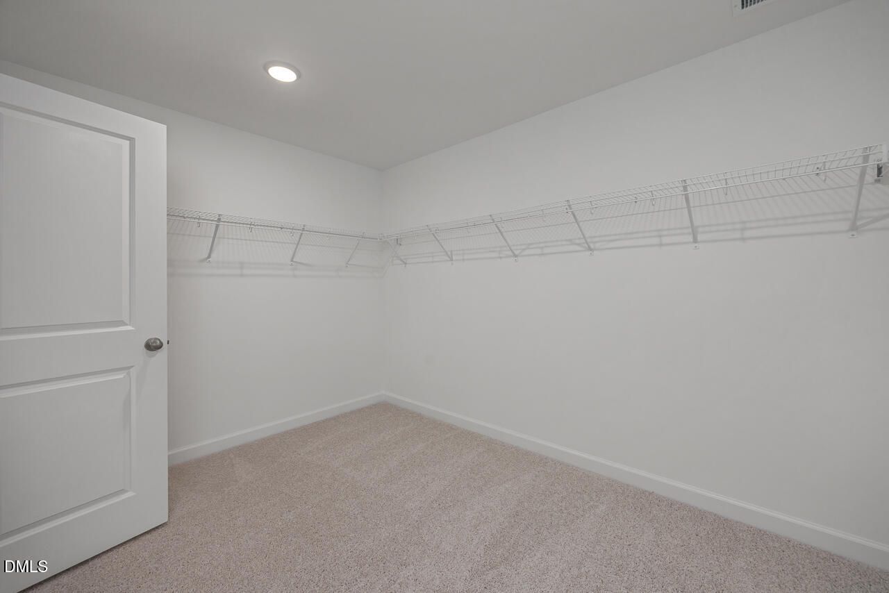 Spacious walk-in closet with wire shelving, white walls, and beige carpet in Davidson Homes The Preston A, Lillington, NC