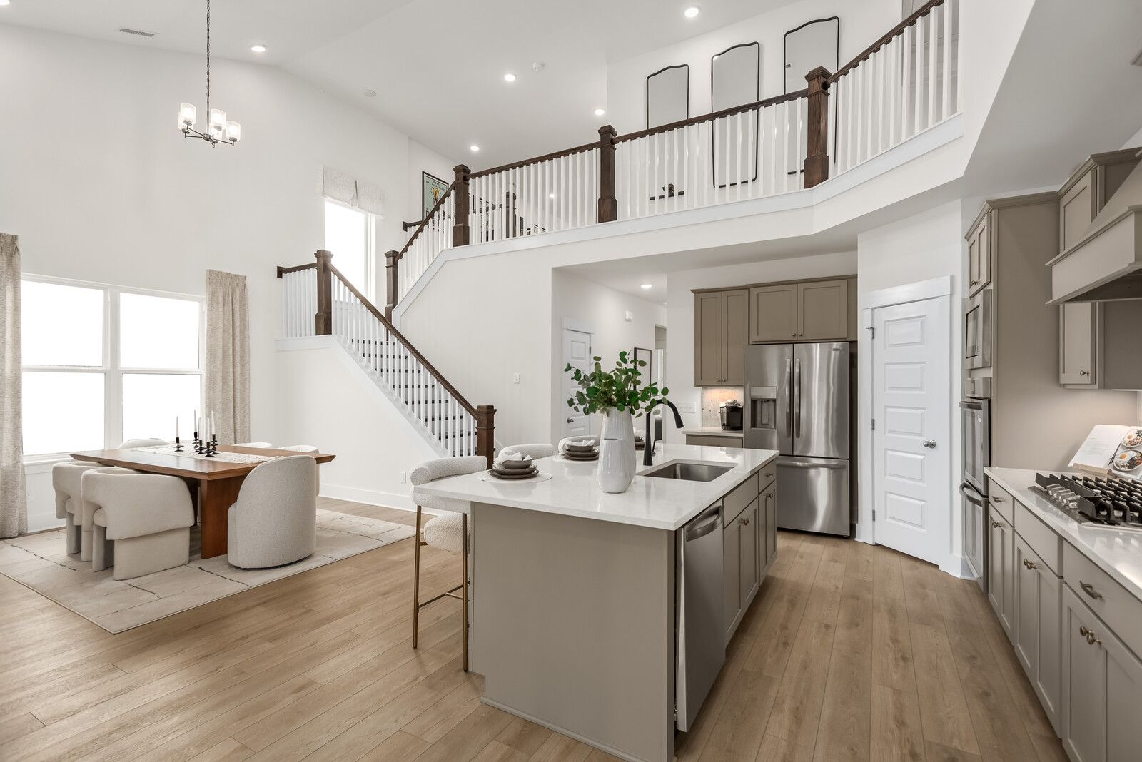 Spacious open-concept kitchen and dining in The Ridgeport E with gray island, stainless appliances, wooden floors, and two-story staircase