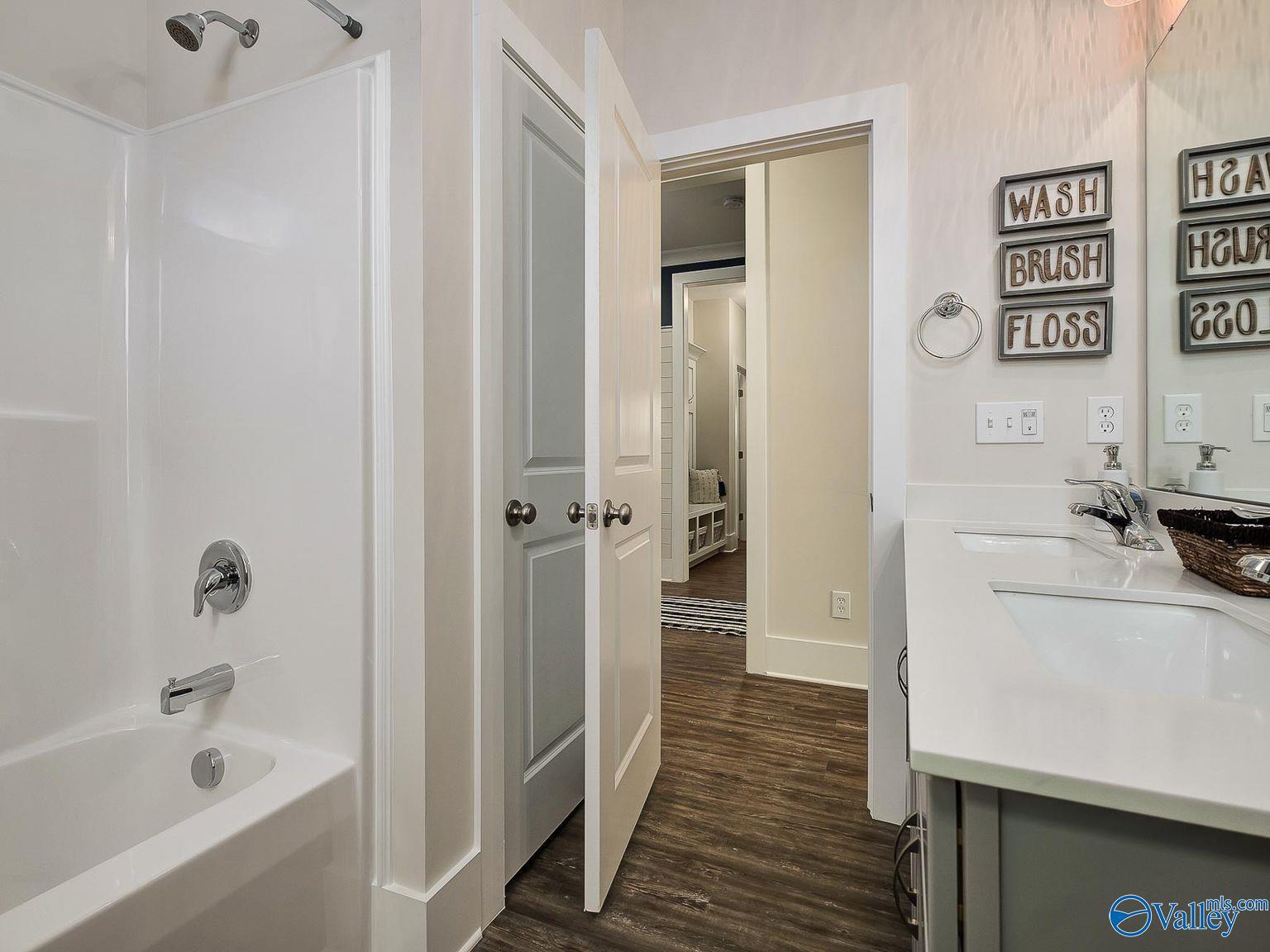 Modern bathroom with white bathtub, glass shower, double vanity and fun wall signs in Davidson Homes The Everett, Toney AL