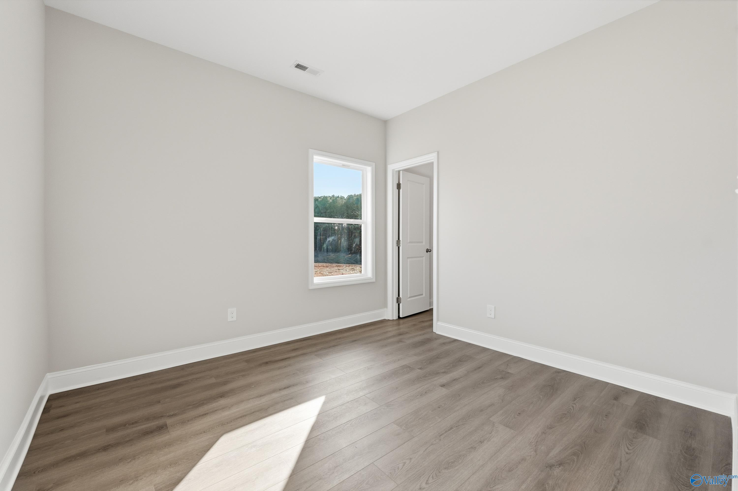 Bright secondary bedroom with light gray walls, large window, and wood-look flooring in Davidson Homes The Daphne C, Arab, Alabama