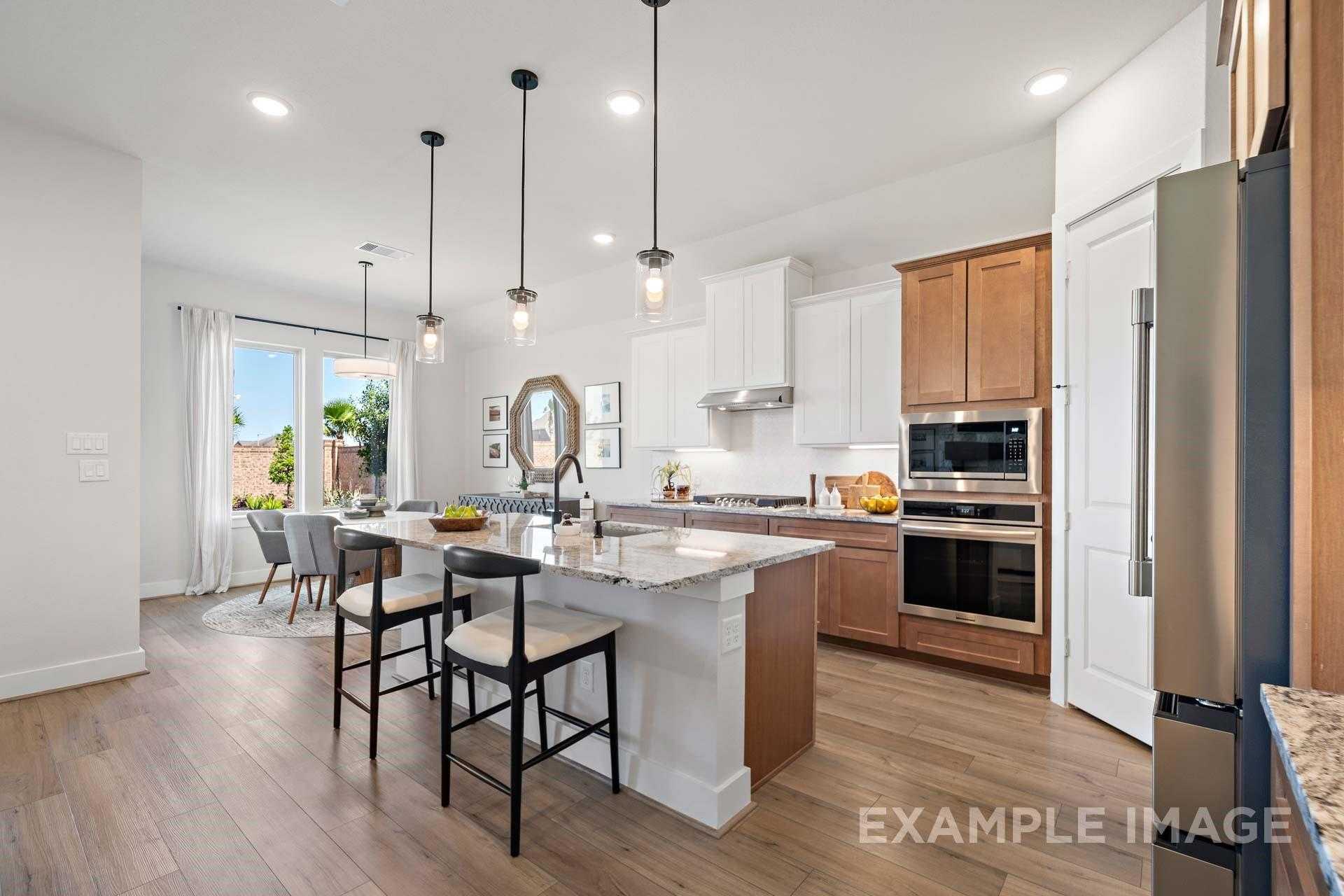 Modern open-concept kitchen with white cabinets, quartz island, stainless appliances, and pendant lights in Davidson Homes The Edward A, Lago Mar, Texas City