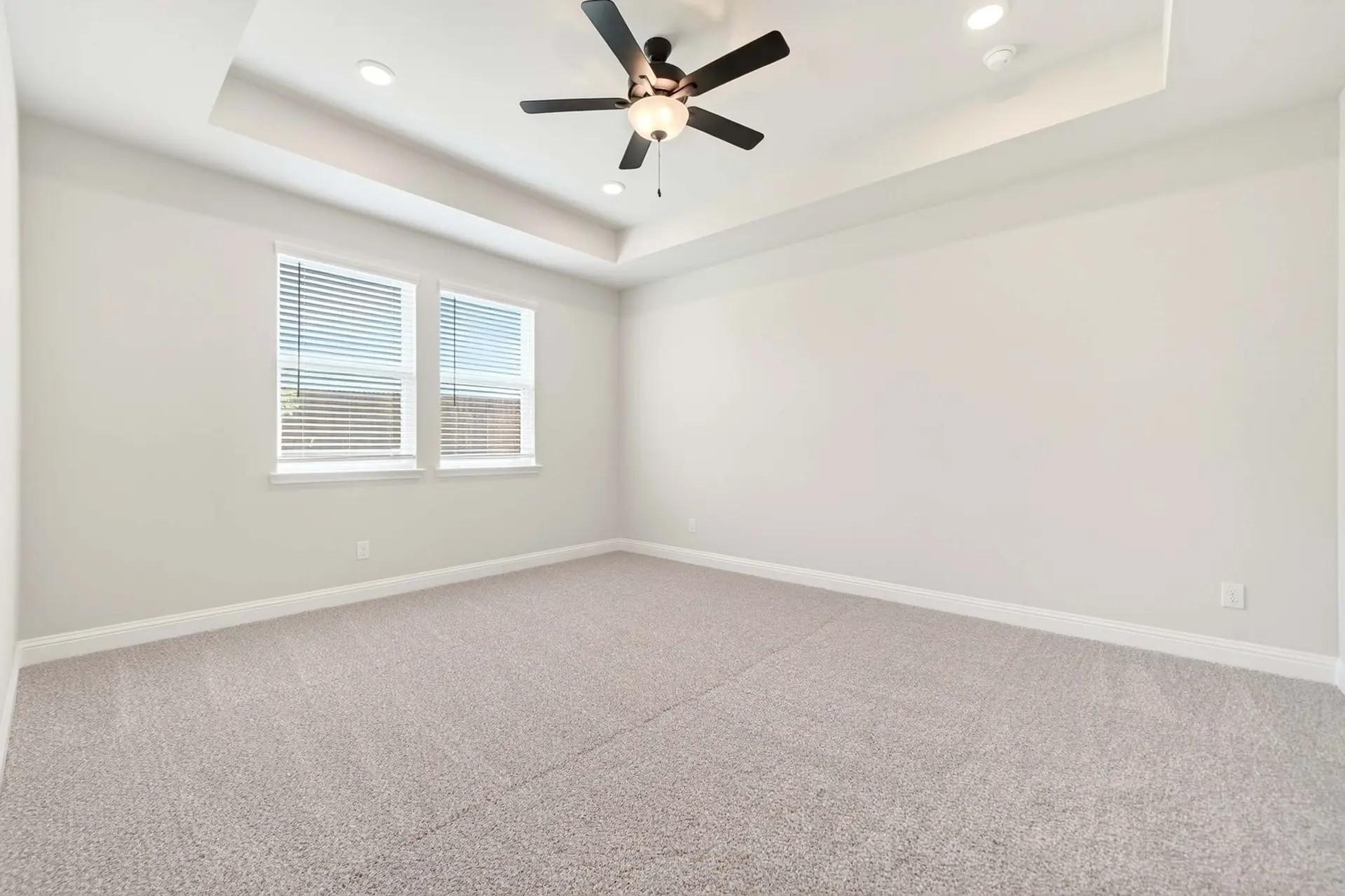 Spacious bedroom with tray ceiling and ceiling fan in The Holly C floor plan by Davidson Homes in Heartland, Texas.