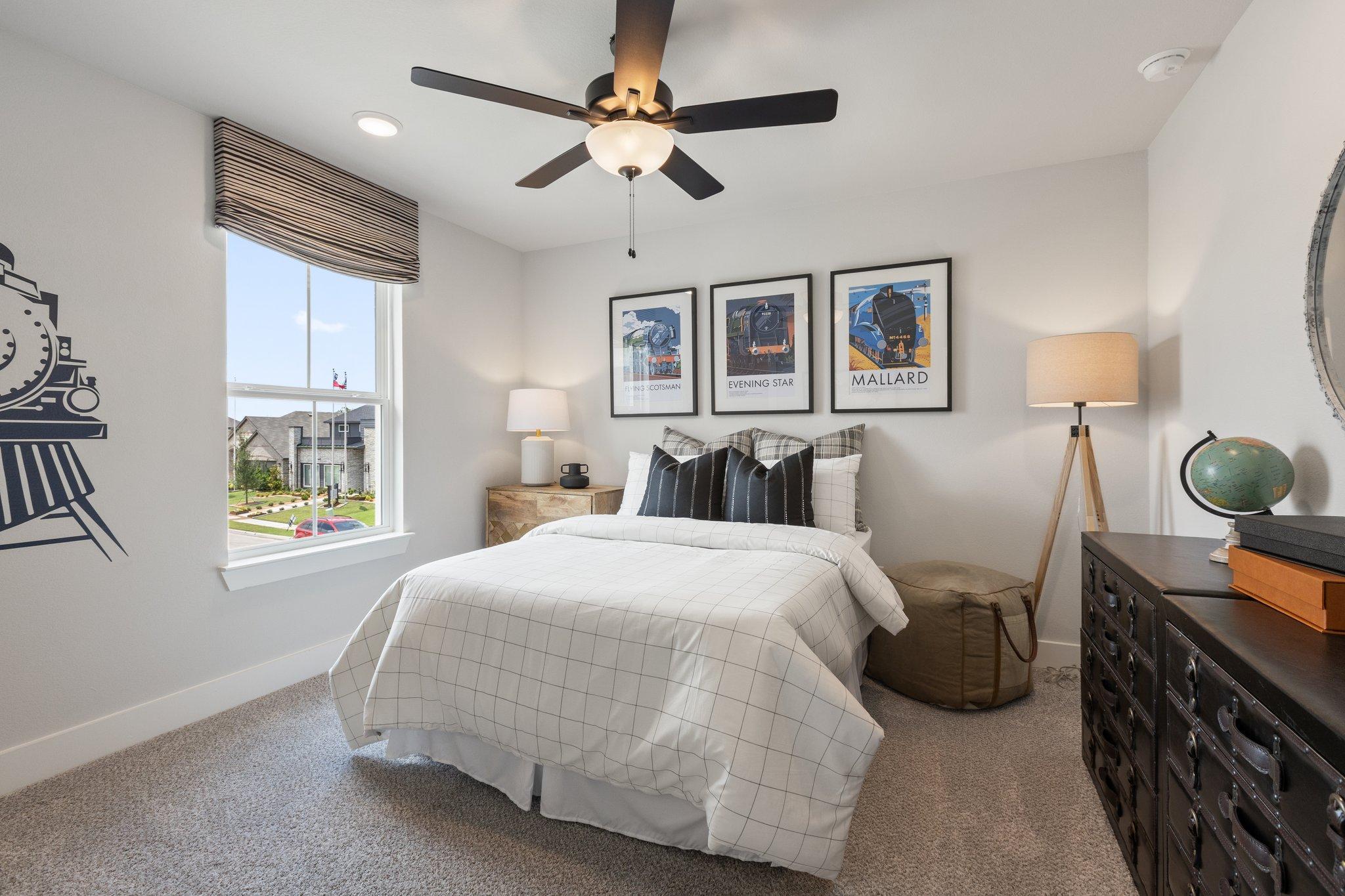 Cozy bedroom interior at Mercer Meadows in Royse City, Texas featuring white bedding, ceiling fan, train wall mural, and neighborhood view