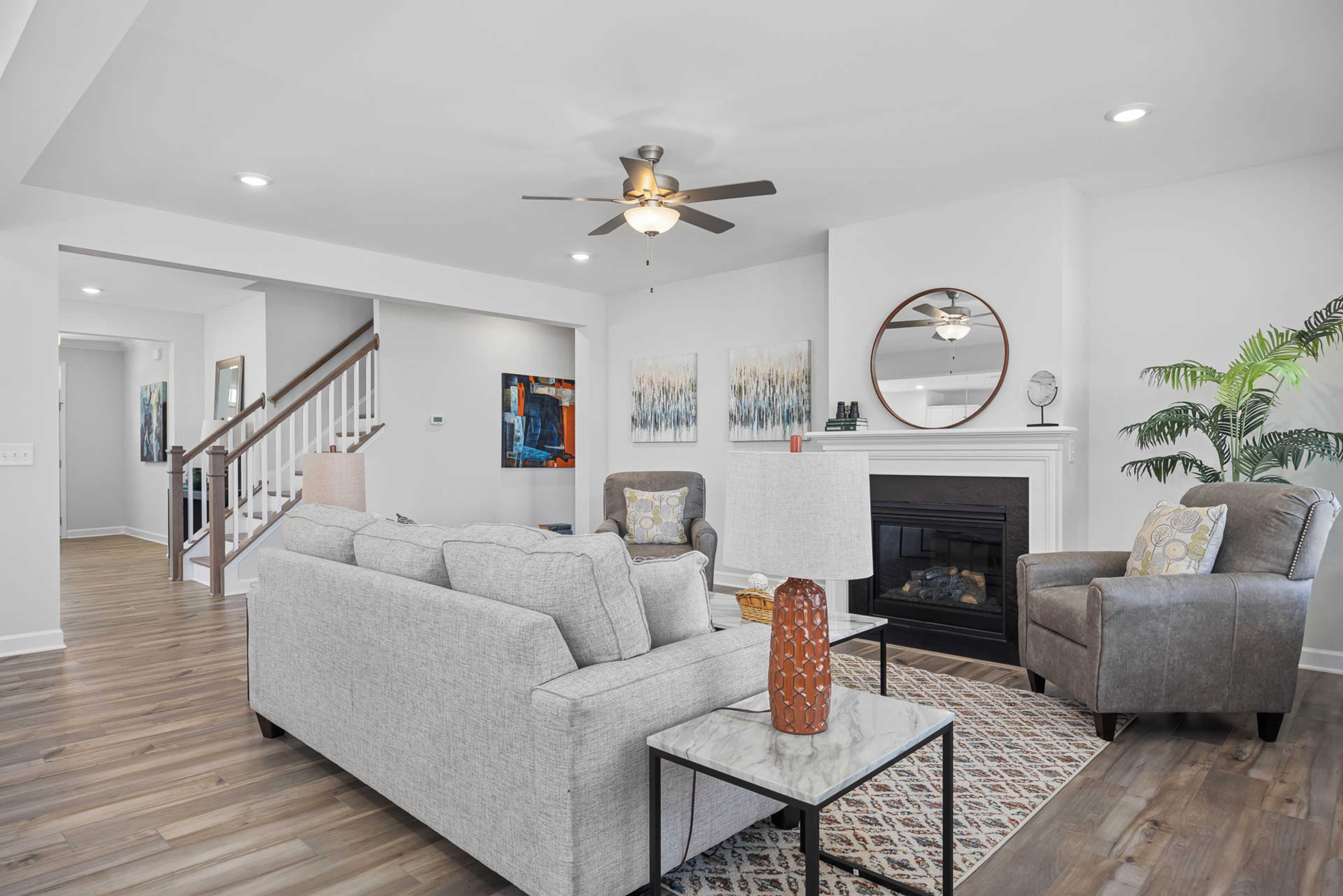 Spacious open-concept living room at Bentwinds in Fuquay-Varina NC by Davidson Homes with gray sofa, gas fireplace, hardwood floors, and ceiling fan