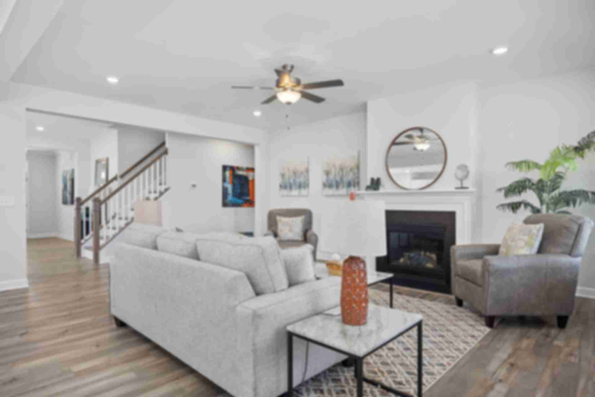 Spacious open-concept living room at Bentwinds in Fuquay-Varina NC by Davidson Homes with gray sofa, gas fireplace, hardwood floors, and ceiling fan