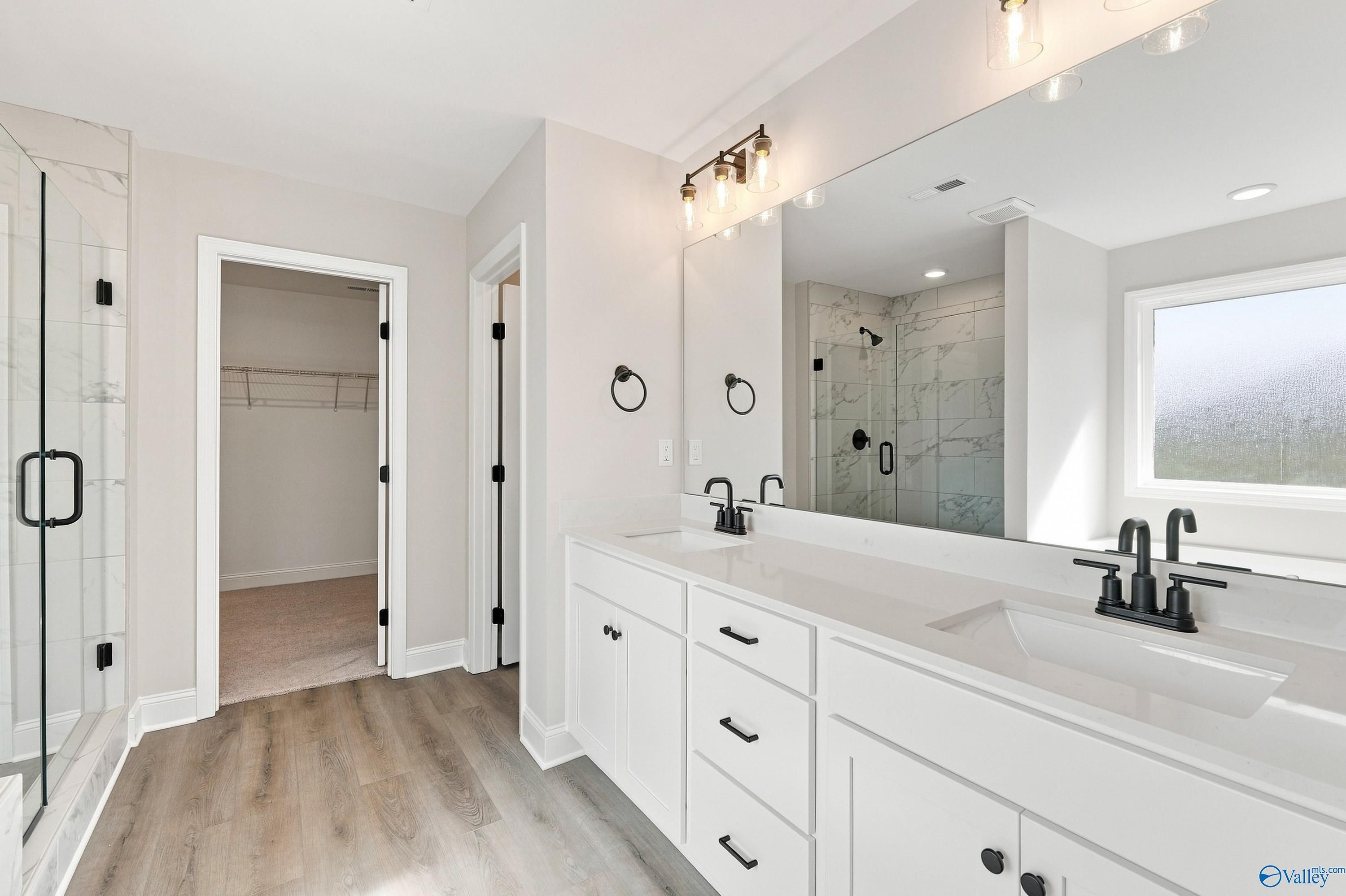 Primary bathroom with double vanity, matte black fixtures, marble tile shower, and wide mirror in Davidson Homes Chelsea B, New Market, AL