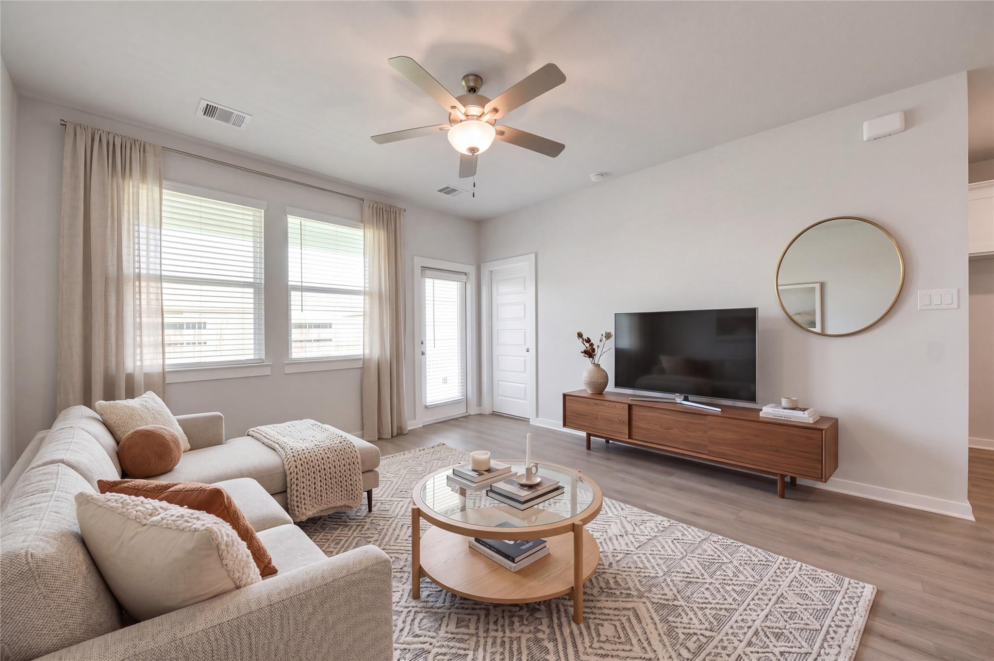Bright living room with ceiling fan, sectional sofa, and glass coffee table in Davidson Homes The Costa A, Emberly, Beasley, Texas