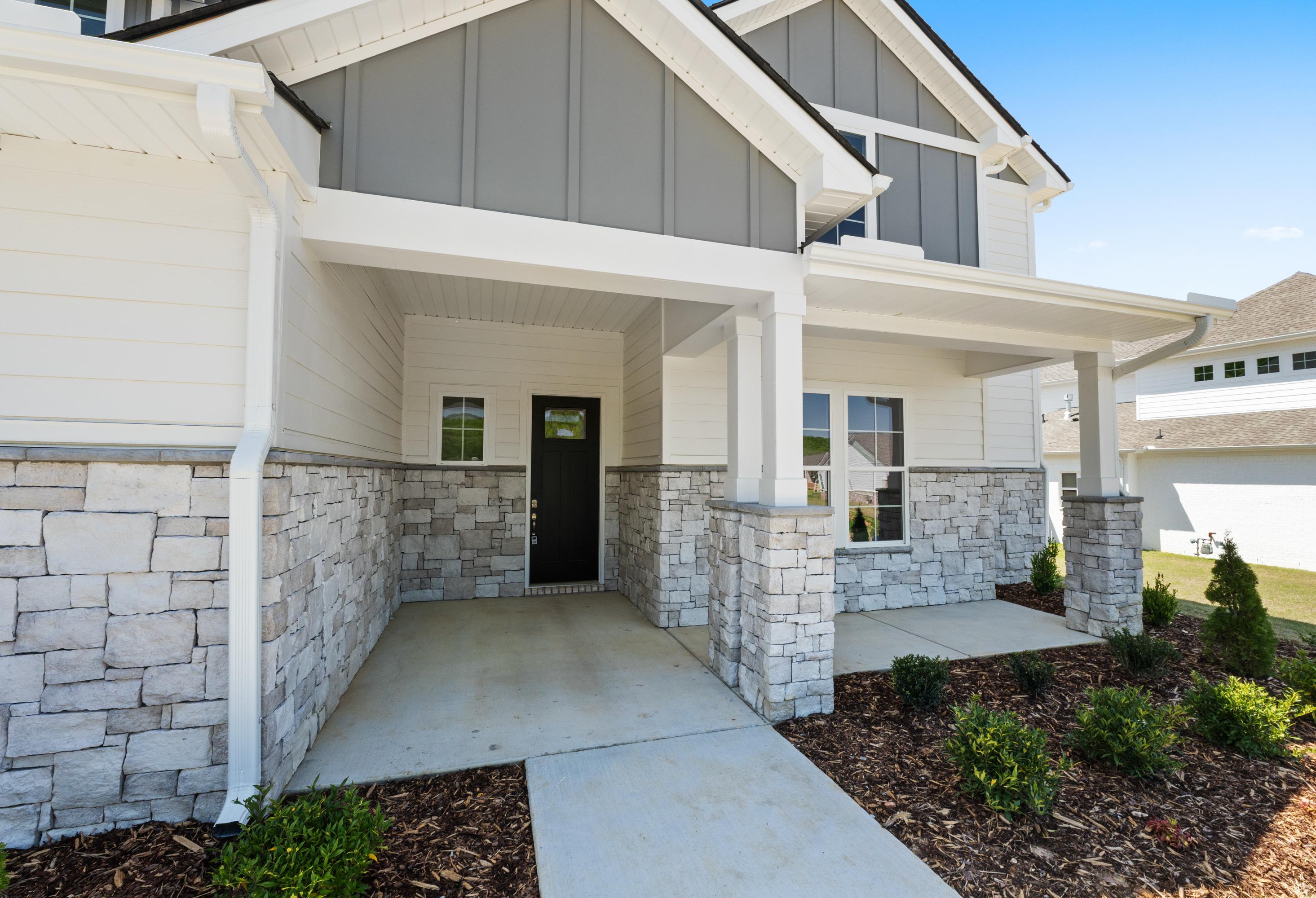 Modern Haven D home exterior with gray siding, stone accents, covered porch, black door, and landscaped entry