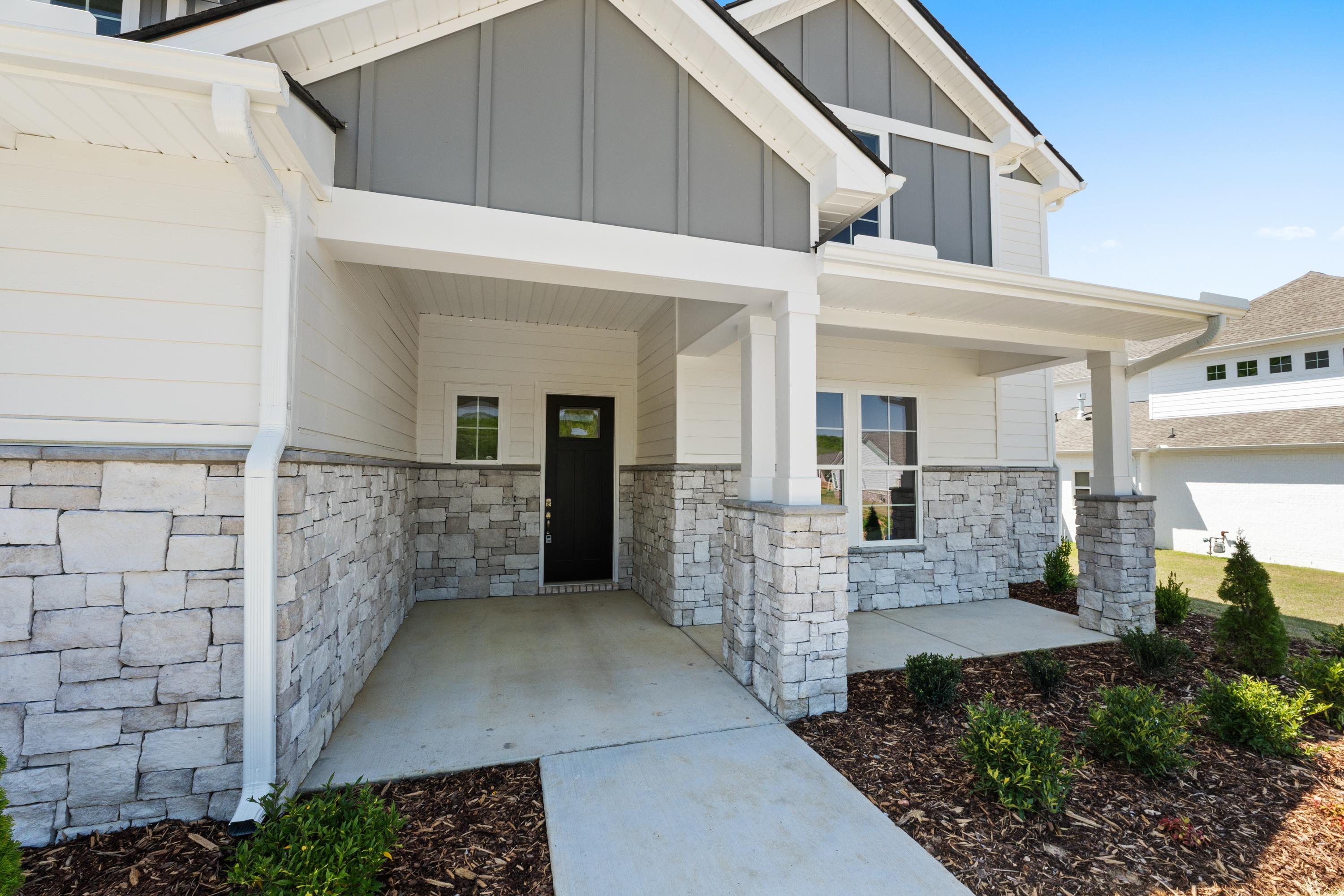 Modern Haven D home exterior with gray siding, stone accents, covered porch, black door, and landscaped entry