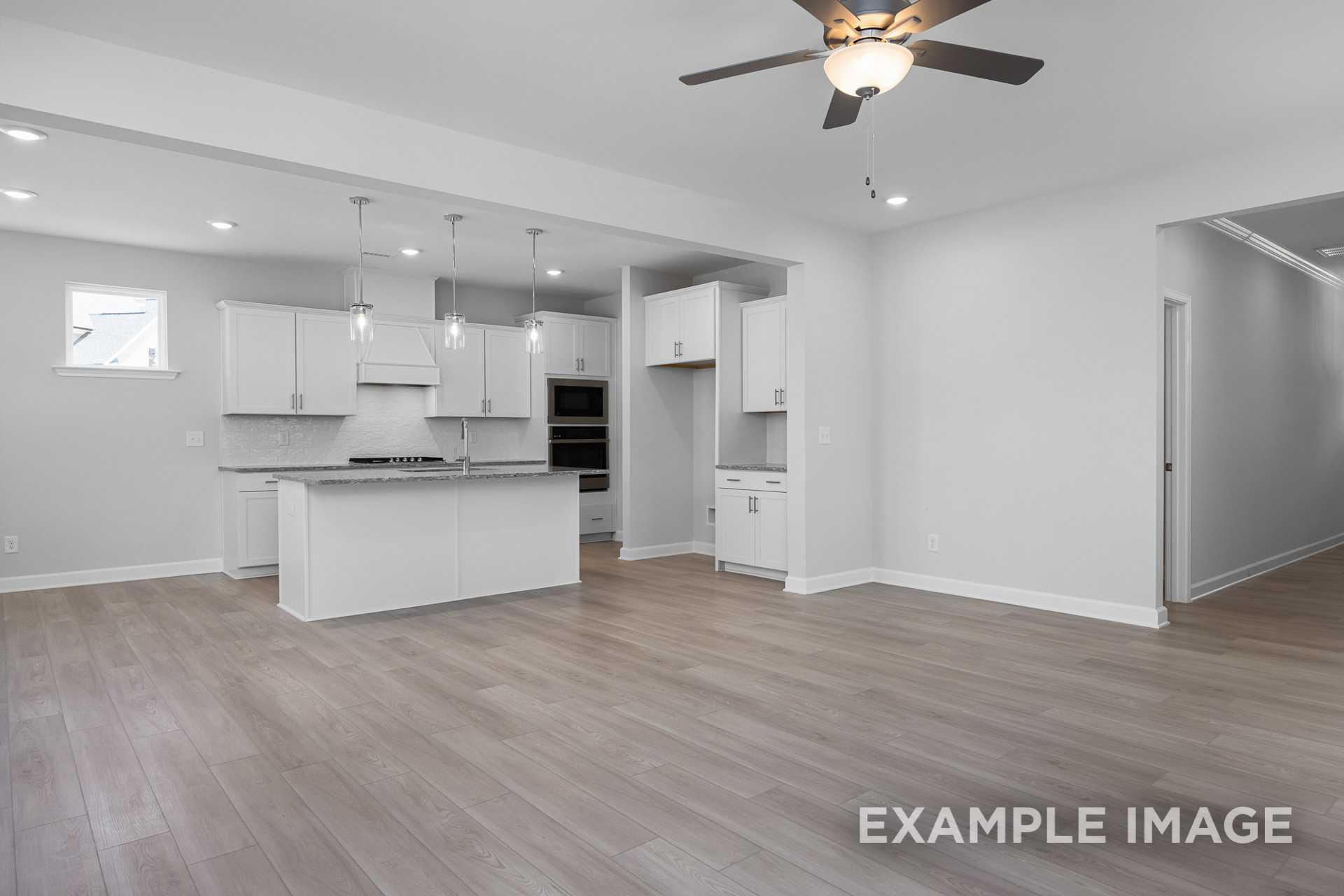 Spacious modern kitchen in The Gavin C home design featuring white cabinetry, large center island, double ovens, and open layout