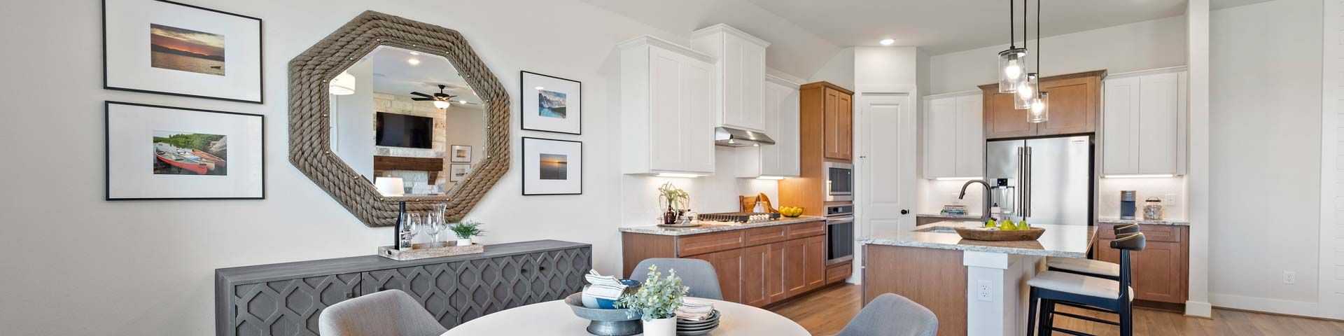 Modern dining area with white round table, gray upholstered chairs, and open kitchen in new Magnolia home