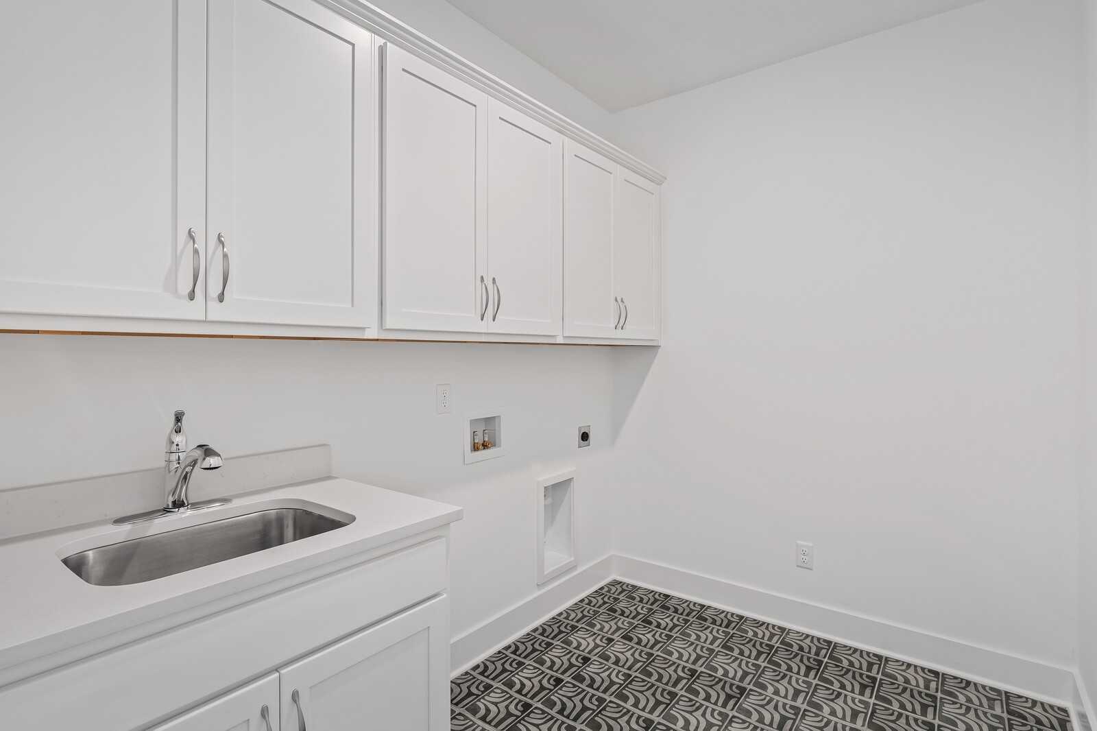 Modern laundry room with white shaker cabinets, stainless sink, and black-white patterned tile floor in Davidson Homes The Hawkins, Murfreesboro, TN