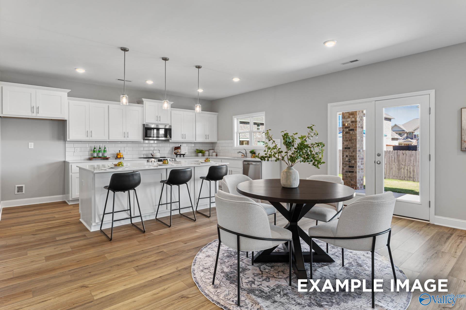 Open-concept kitchen with white cabinets, stainless appliances, island bar, and dining area via French doors in Davidson Homes Chelsea B, Toney, AL