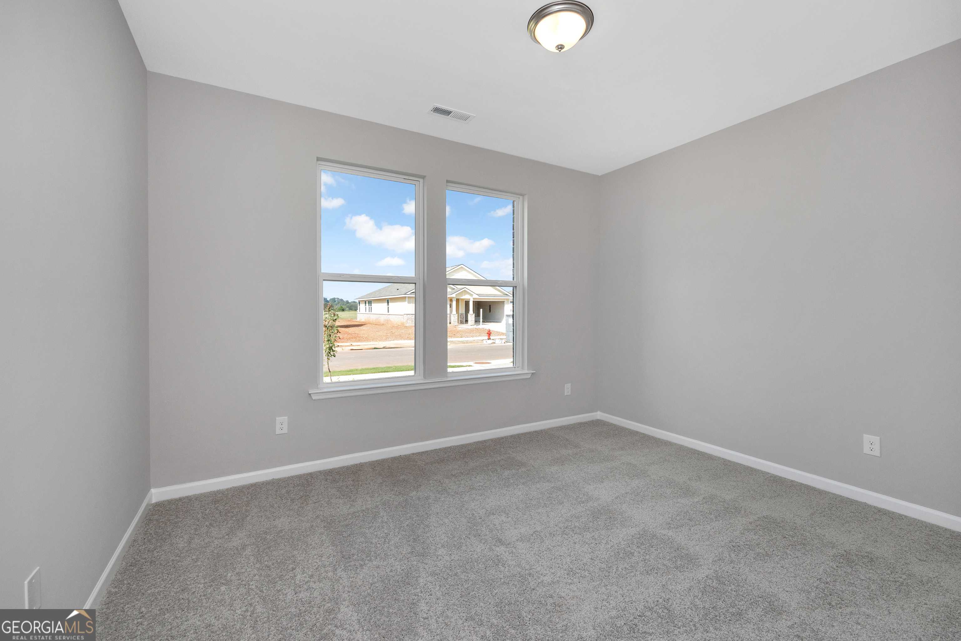 Bright secondary bedroom with gray walls, carpet flooring, and large windows in Evermore Homes The Luna, Perry, GA