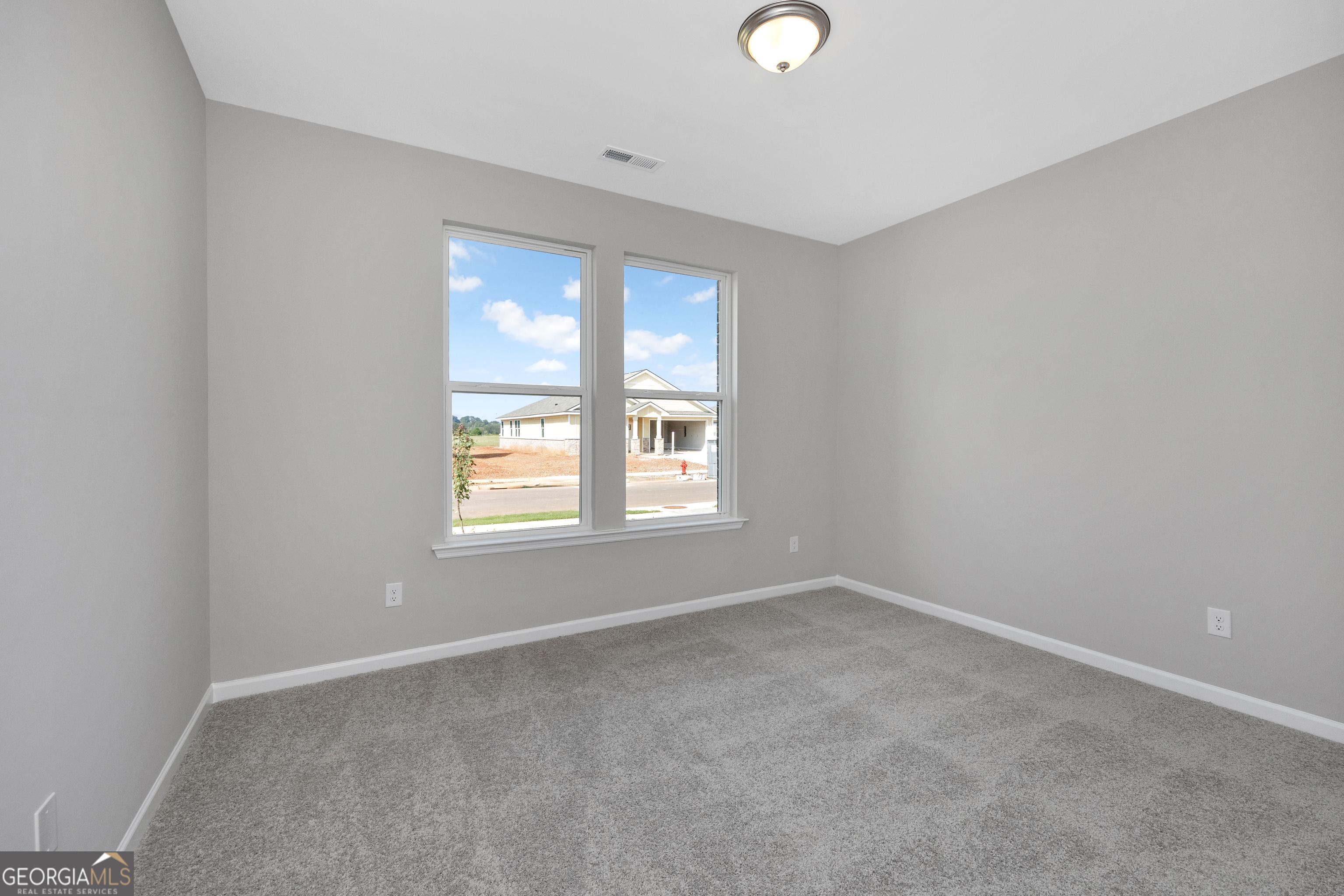 Bright secondary bedroom with gray walls, carpet flooring, and large windows overlooking neighborhood in The Luna home, Ivy Glen, Perry, Georgia