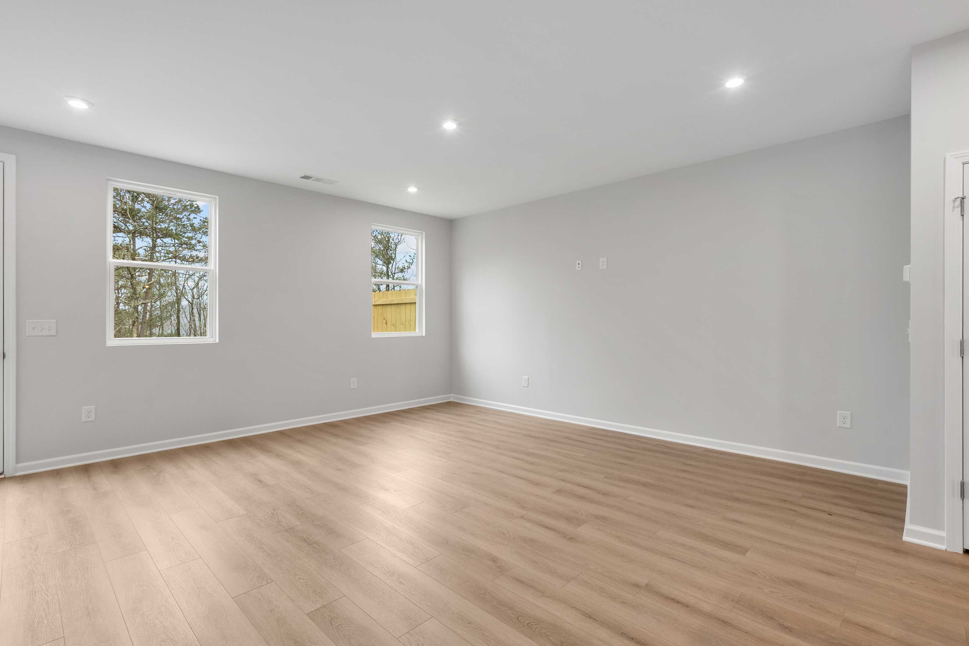 Spacious empty master bedroom in The Durant A home with light gray walls, oak hardwood floors, and large windows overlooking pines