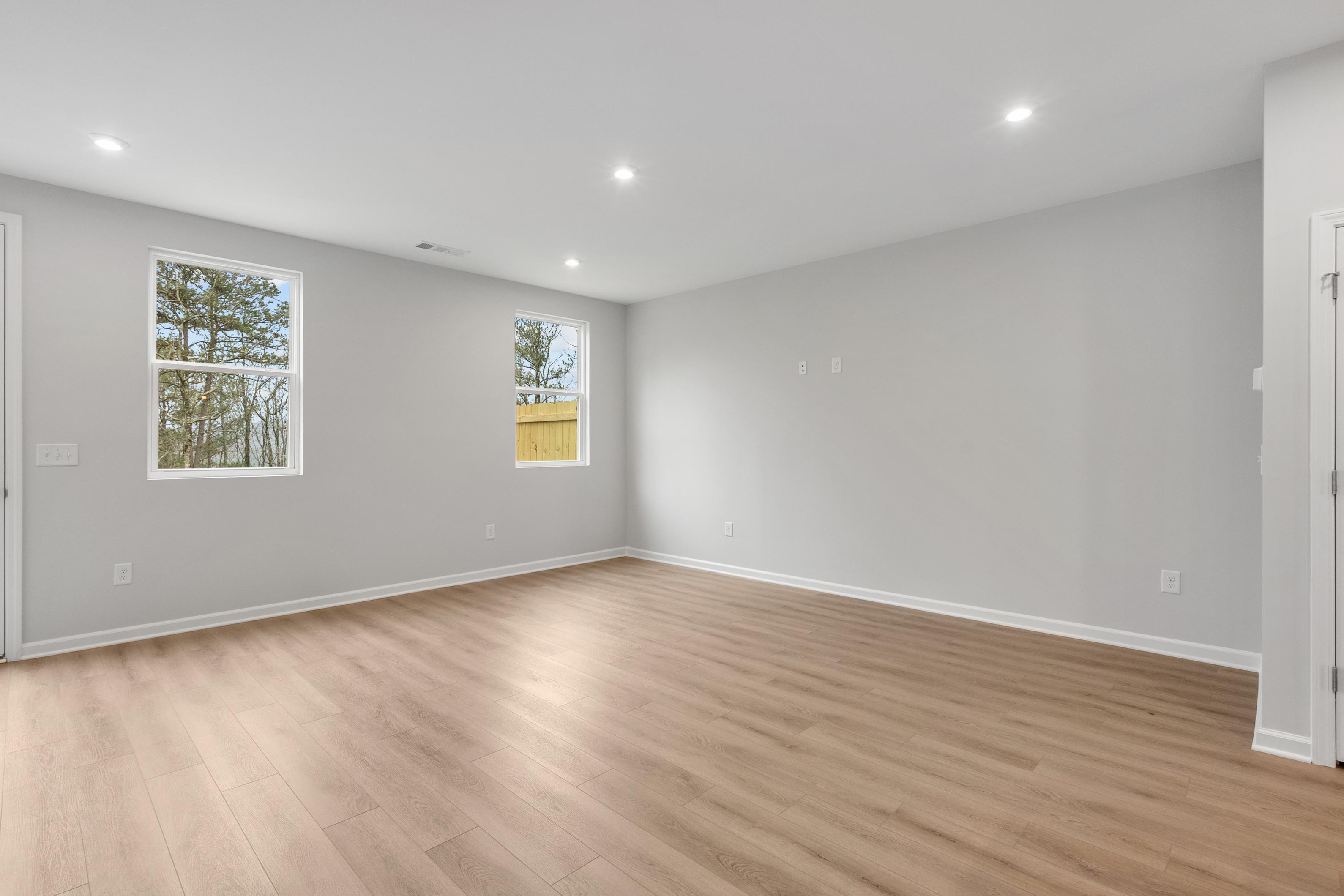 Spacious empty master bedroom in The Durant A home with light gray walls, oak hardwood floors, and large windows overlooking pines