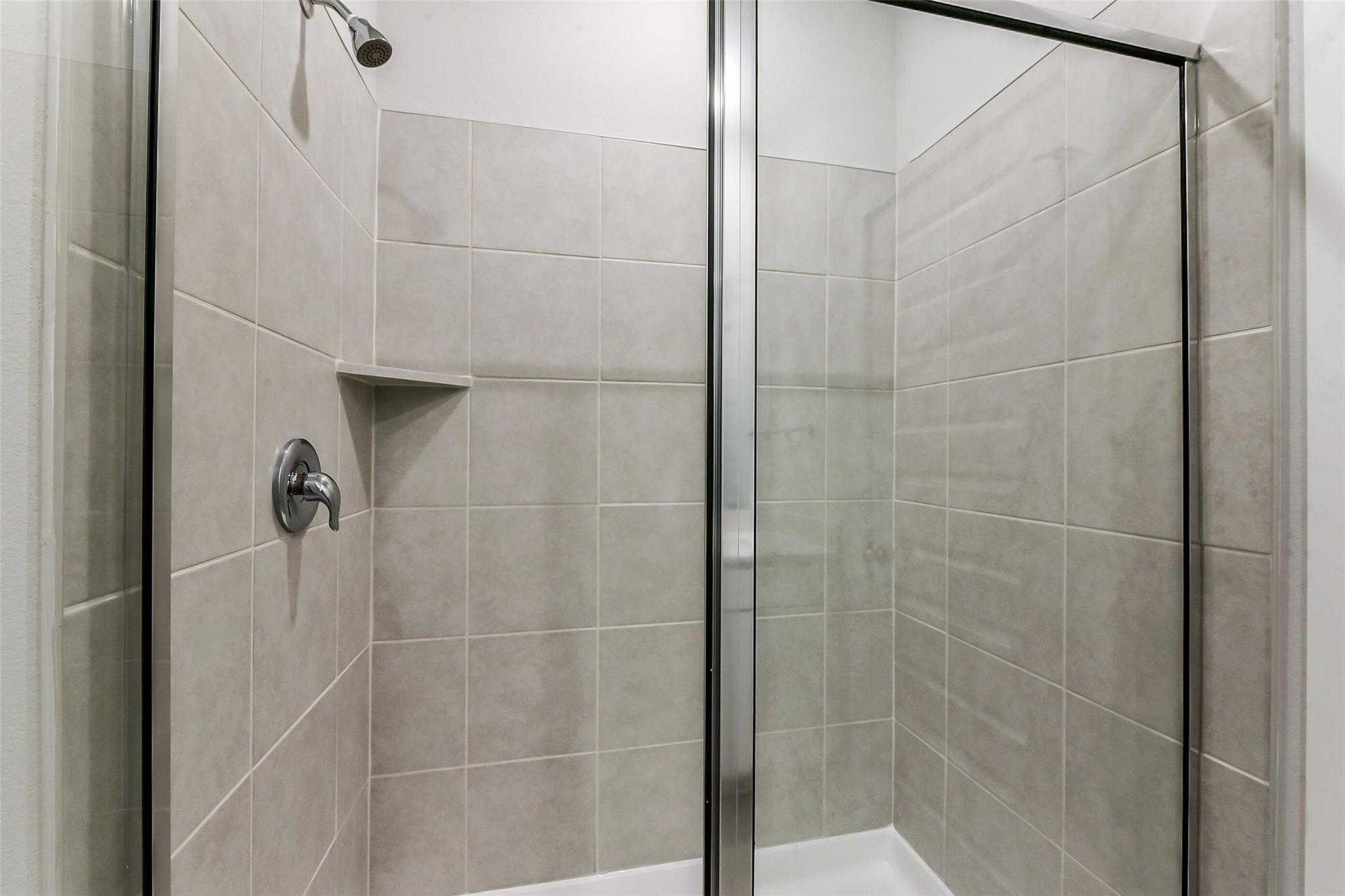 Modern glass-enclosed shower with subway tile walls, niche shelf, and chrome fixtures in Davidson Homes The Frio F bathroom, Dayton Texas