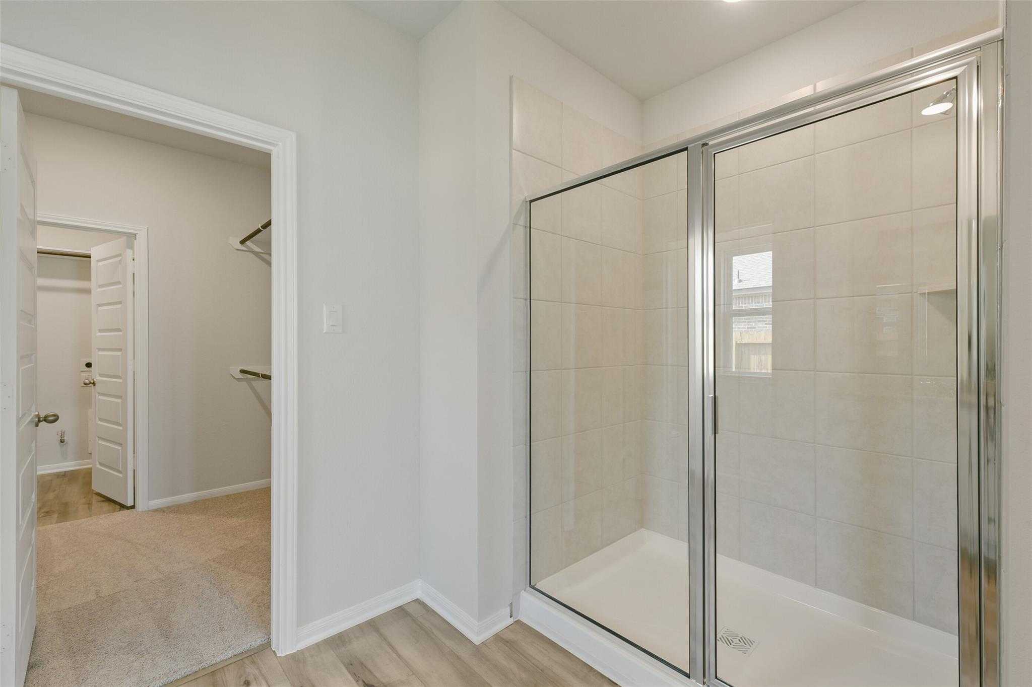 Modern master bathroom featuring frameless glass walk-in shower and adjacent walk-in closet in Davidson Homes The Laguna B, Dayton, Texas