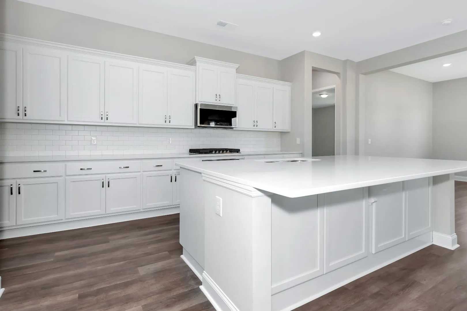 Modern kitchen in The Arcadia M showcasing white shaker cabinets, large quartz island, subway tile backsplash, and open layout