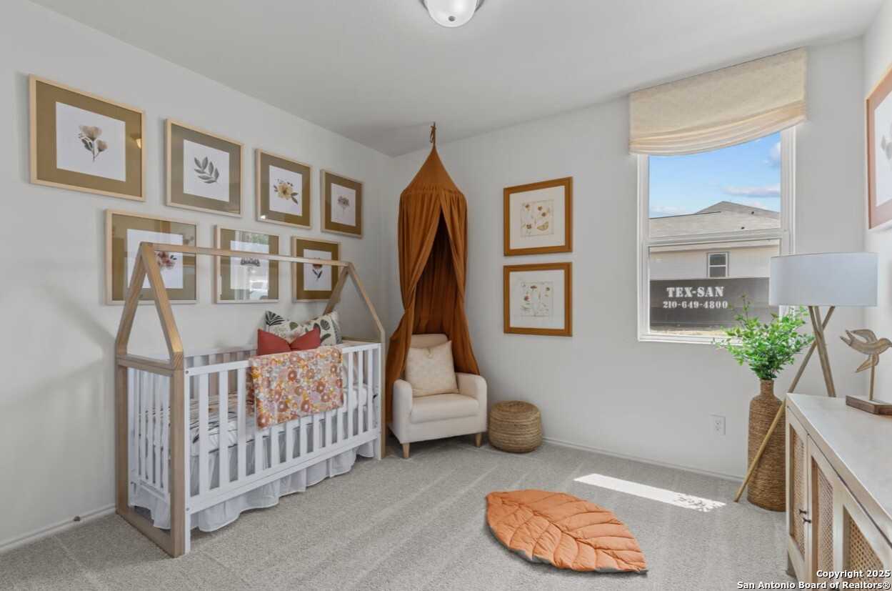 Cozy nursery featuring canopy crib, botanical art frames, armchair, and potted plant in Davidson Homes The Daphne J, Elmendorf, Texas