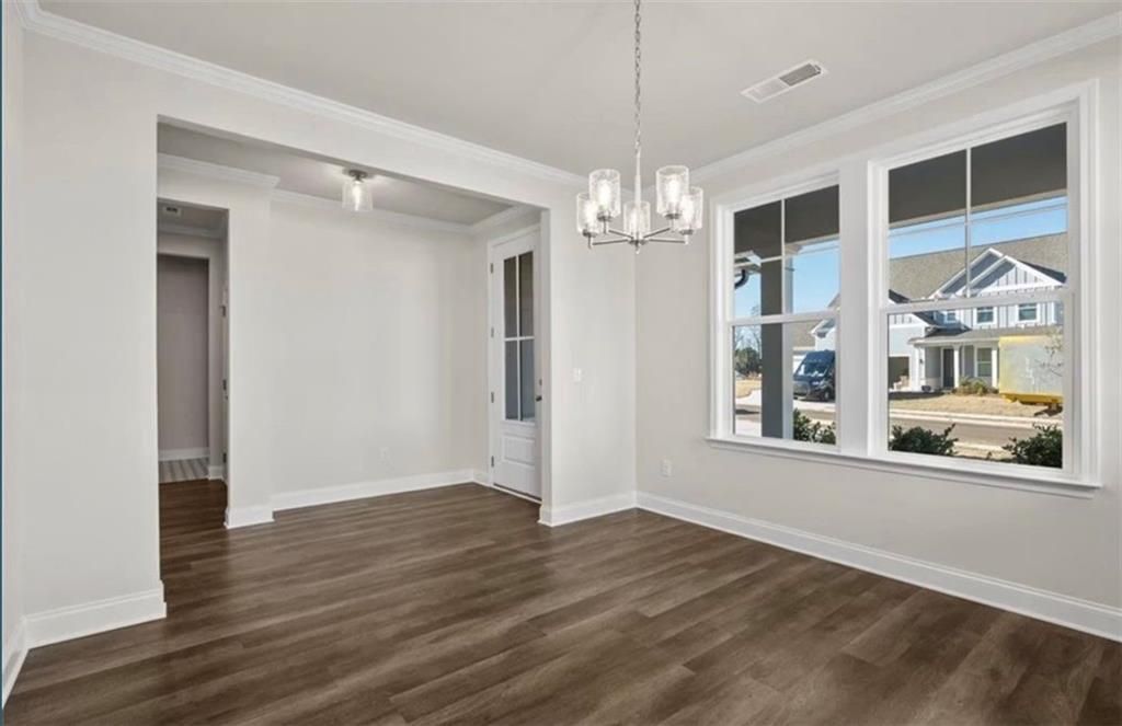 Bright dining area with modern chandelier and wood-look floors in The Ash C floor plan at Wehunt Meadows, Hoschton, GA.