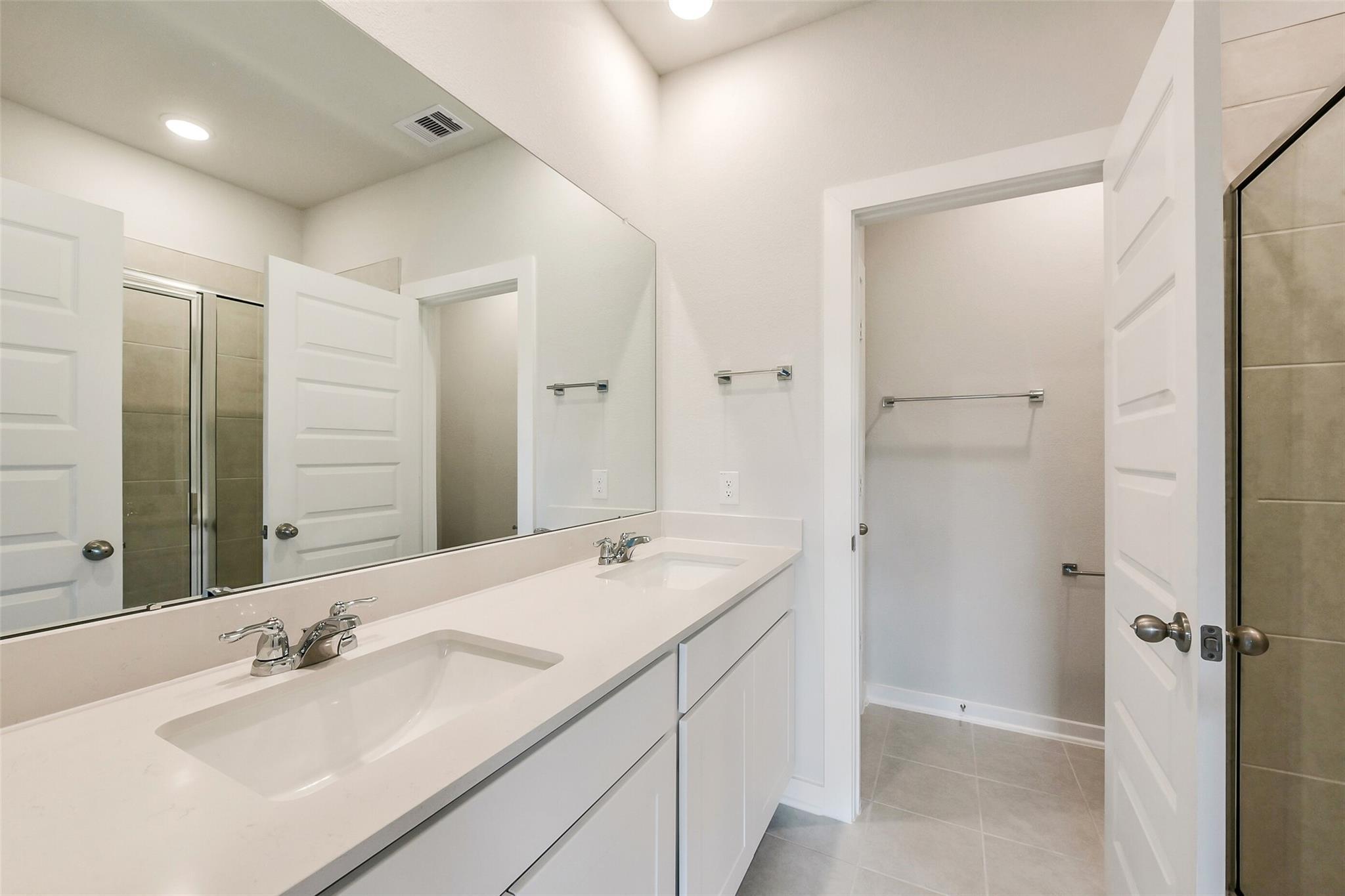 Modern master bathroom with double vanity sinks, mirrors, and white cabinets in Davidson Homes The Frio G, Dayton, Texas