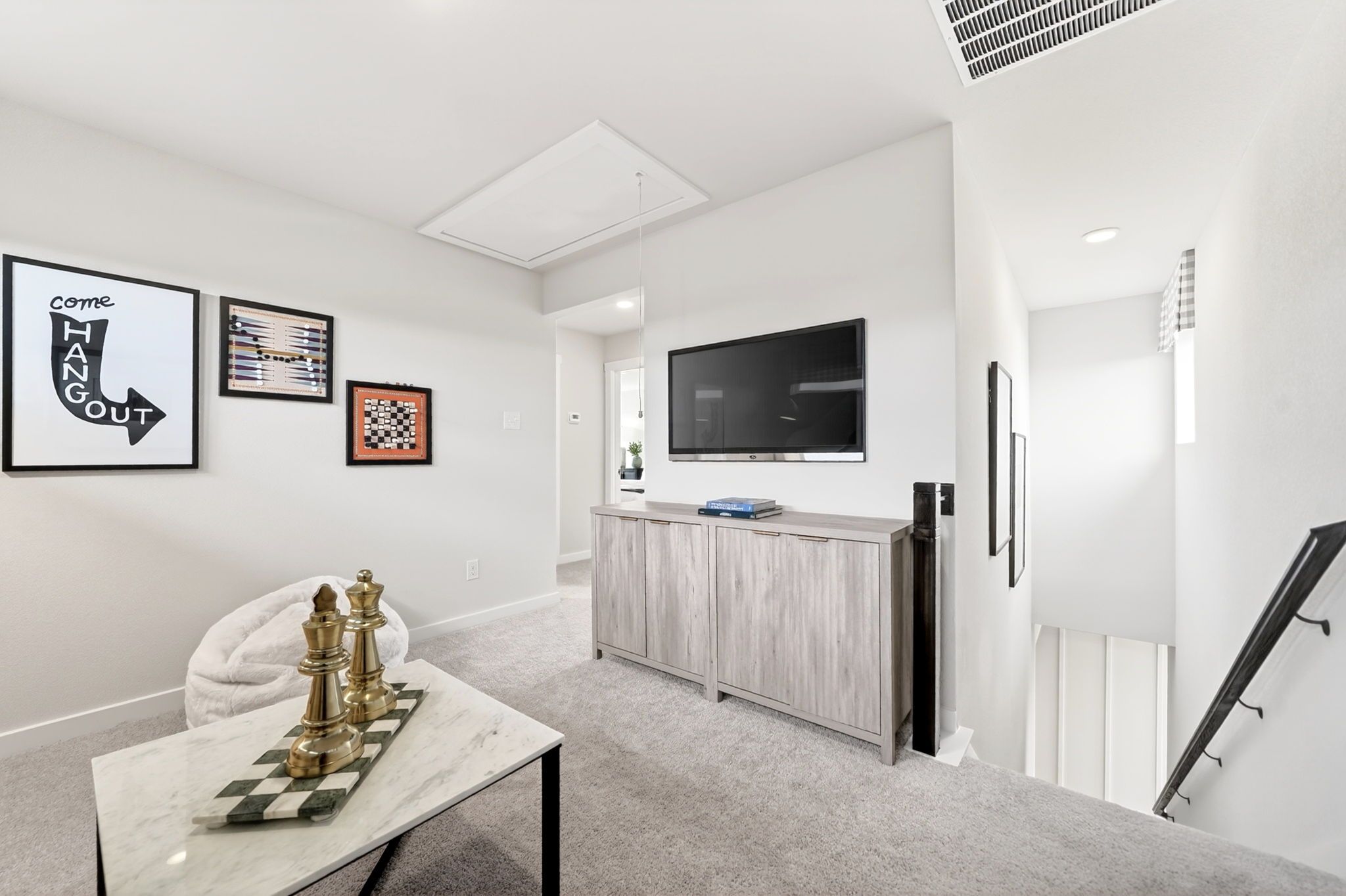 Cozy loft space at Heartland Texas by Davidson Homes with mounted TV, brass chess set on marble table, wall art, and gray carpet