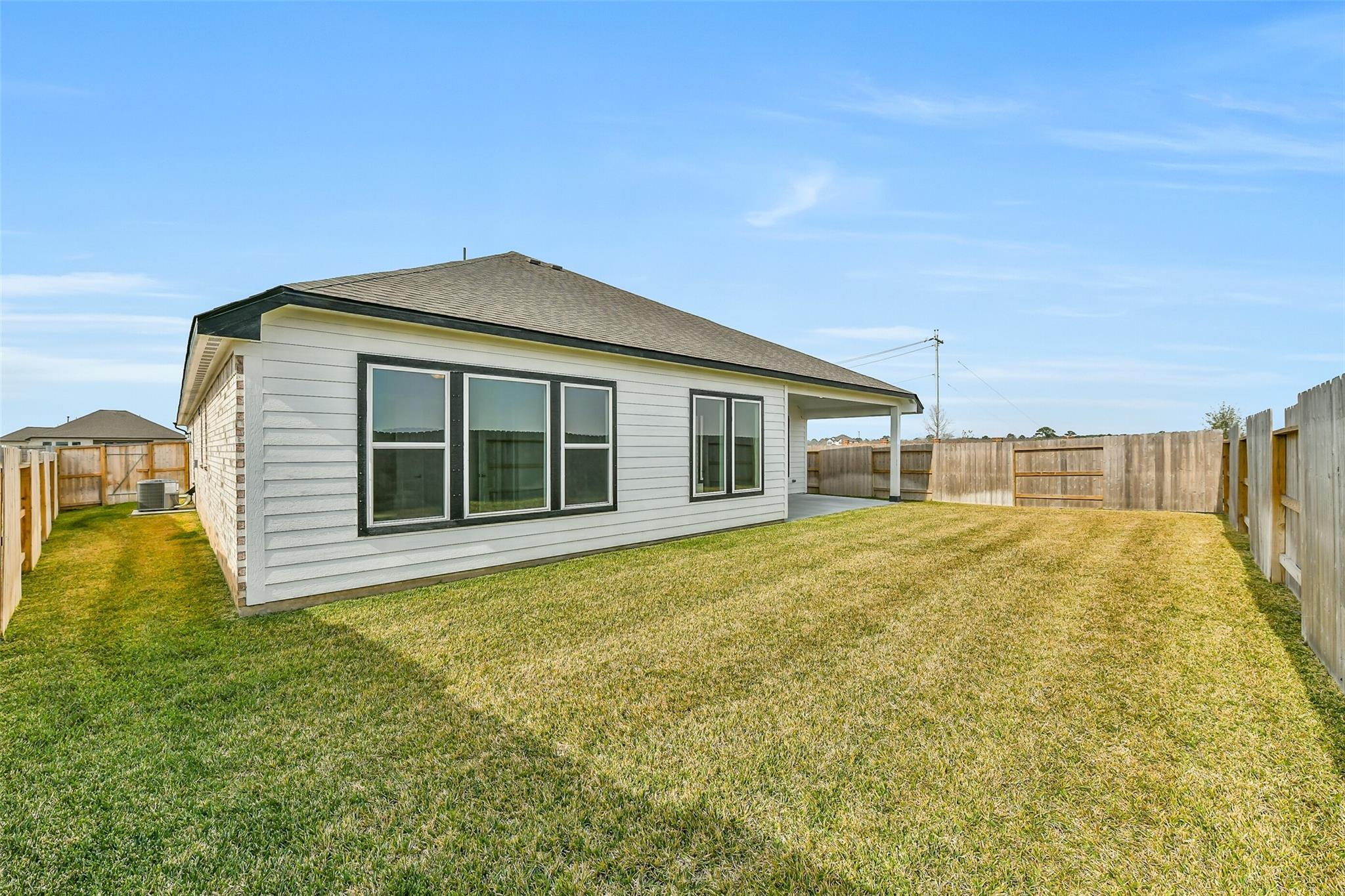 Single-story white home exterior with large black-framed windows, covered garage, and lush green fenced backyard in Lago Mar, Texas City