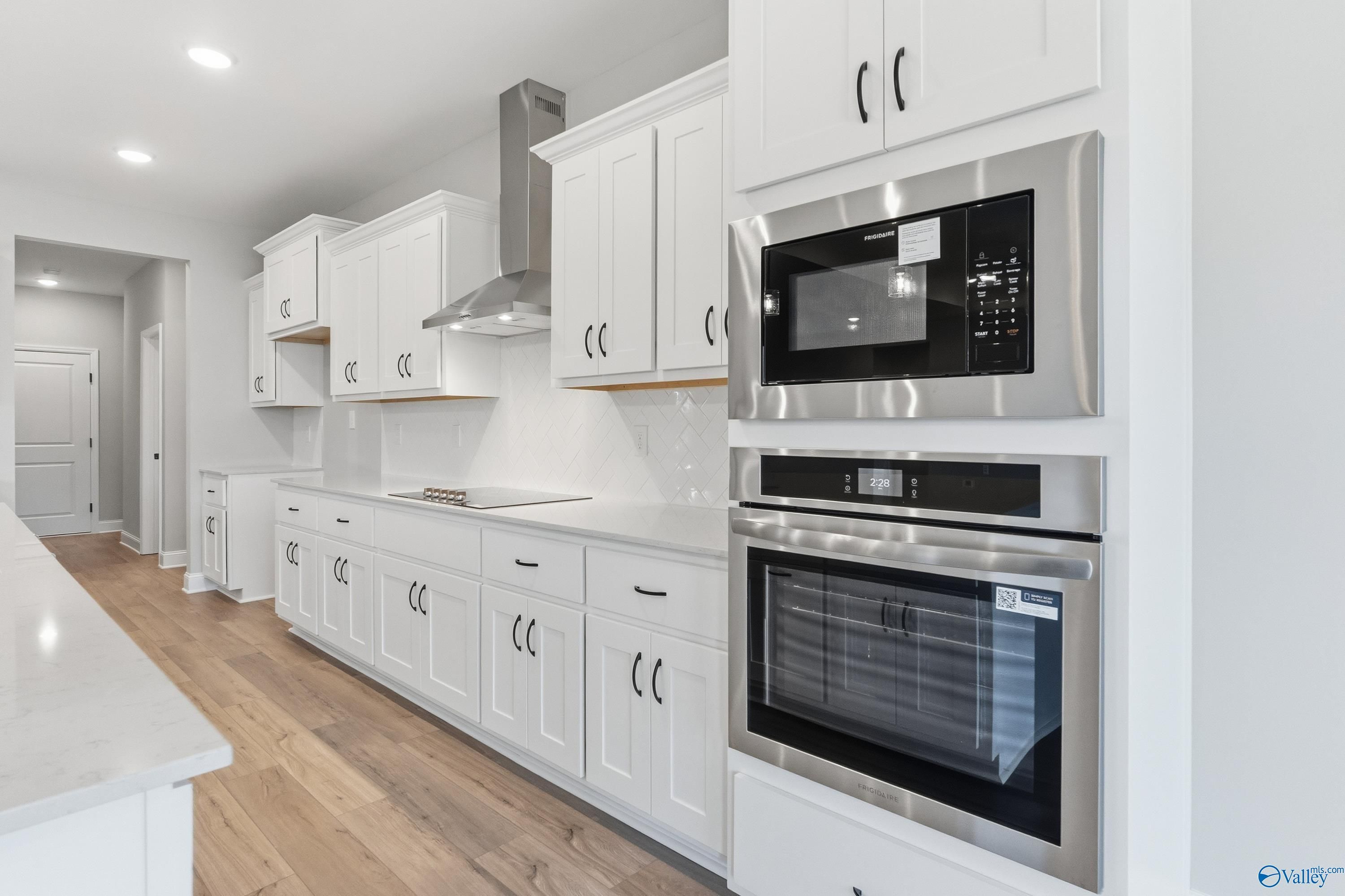 Modern white kitchen with shaker cabinets, stainless steel oven and microwave, quartz island in Davidson Homes The Finleigh, Meridianville, AL