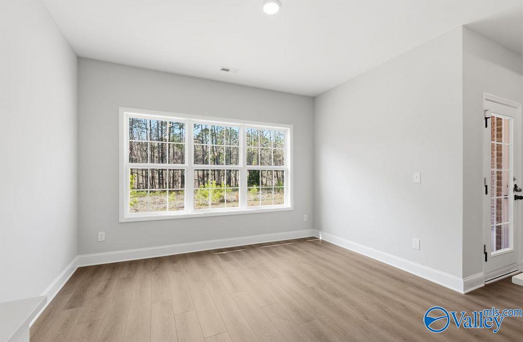 Bright living room with large windows showcasing wooded view, gray walls, wood floors in Davidson Homes The Montgomery B, Hartselle, AL