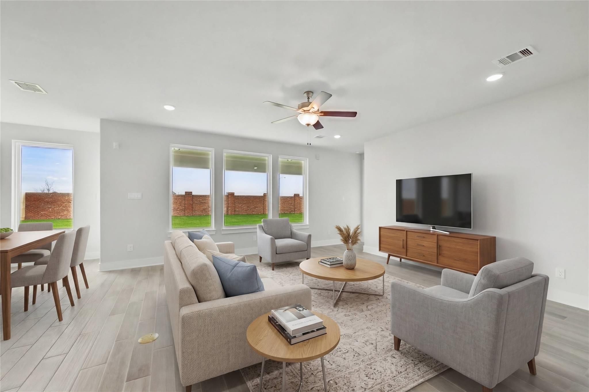 Cozy modern living room with beige L-shaped sofa, armchairs, TV console, large windows to lush backyard in Davidson Homes The Philip A, Lago Mar