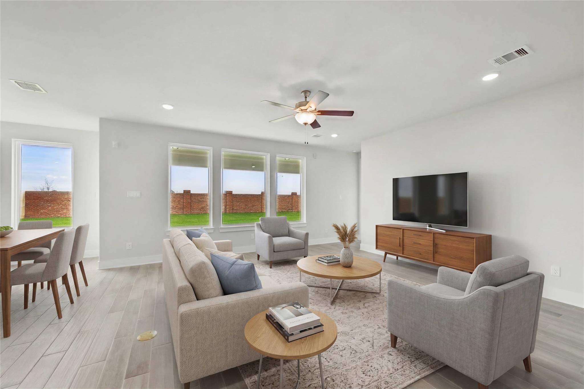 Cozy modern living room with beige L-shaped sofa, armchairs, TV console, large windows to lush backyard in Davidson Homes The Philip A, Lago Mar