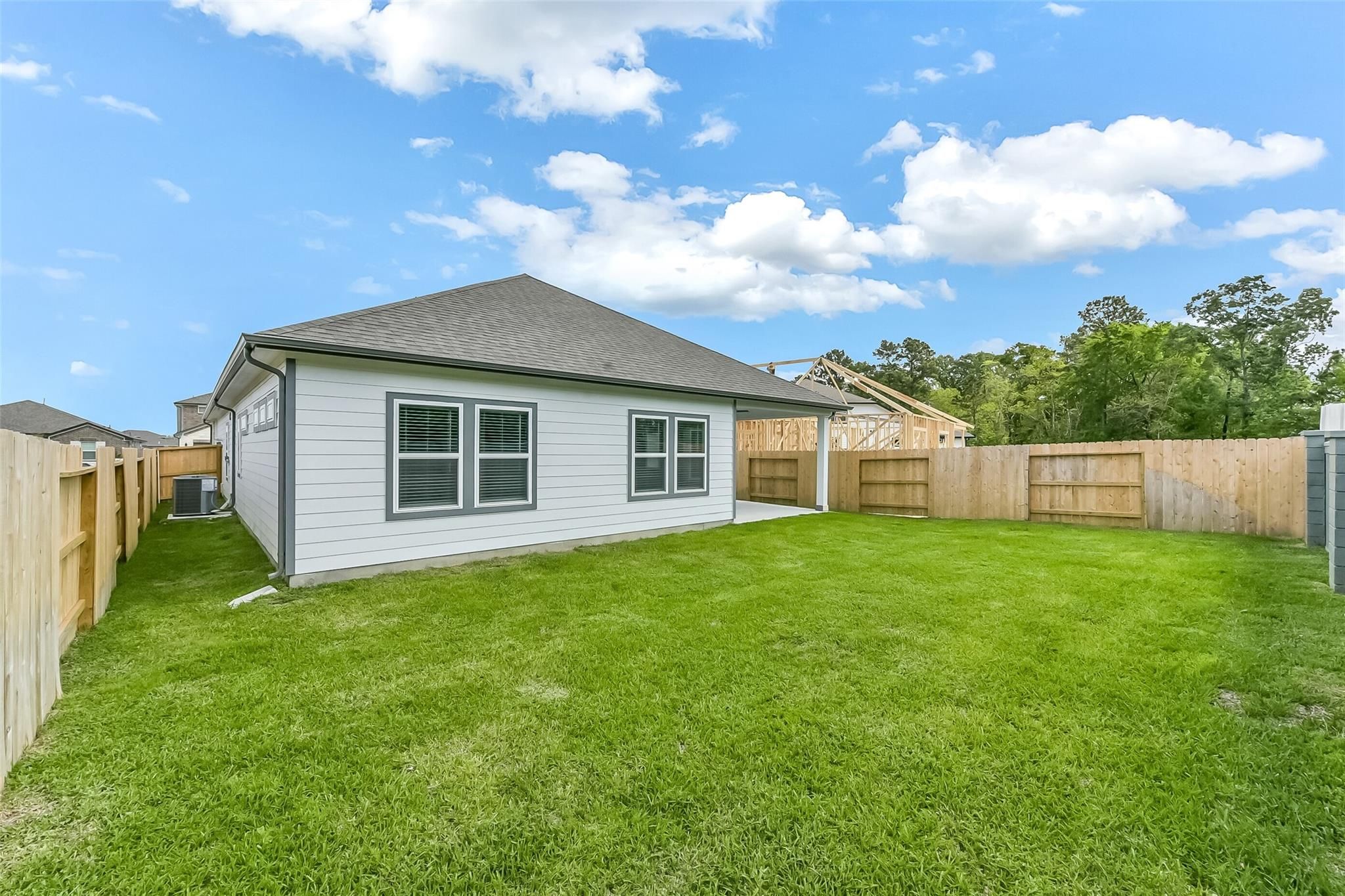 Side view of white single-story The Everett C home with double windows, lush green backyard, and wooden fences in Sundance Cove, Crosby, Texas