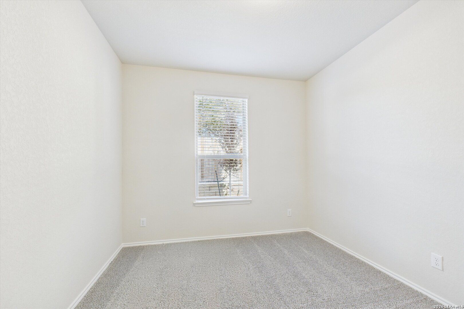 Bright secondary bedroom with neutral beige walls, plush carpet, and large window in Davidson Homes The Gillian B, San Antonio, Texas
